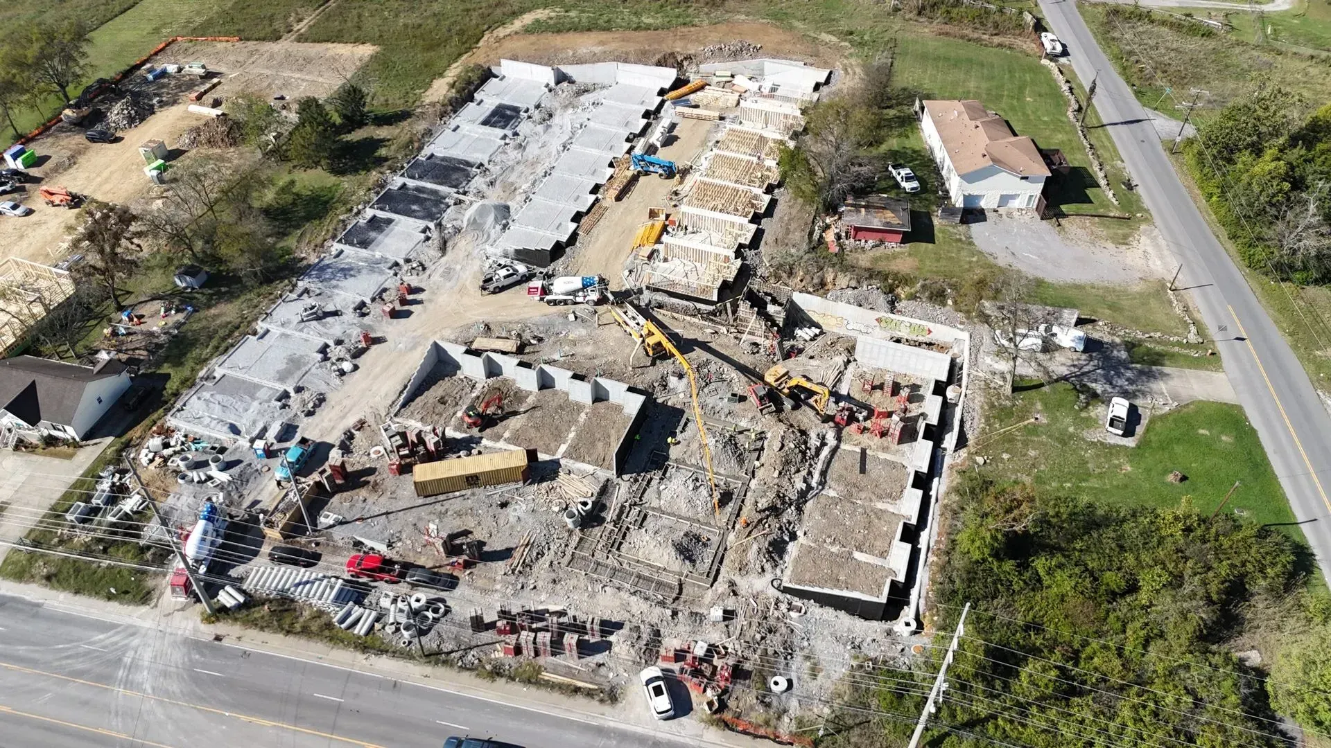 New concrete driveway in front of a light-colored house with a brown roof, under construction on a sunny day.