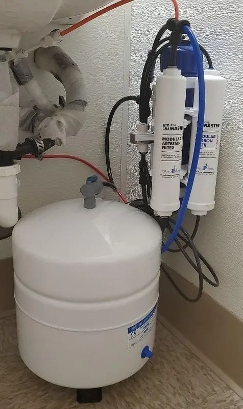 Under-sink water filtration system with white tank, filters, and blue tubing
