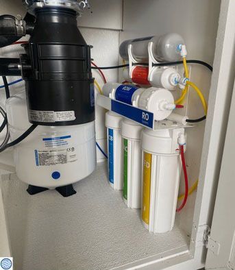 Under-sink reverse osmosis water filtration system with black tank and white filter cartridges.