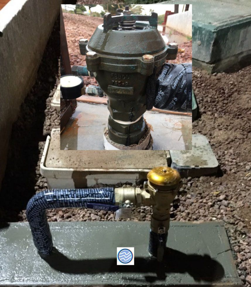 Water meter and valve assembly in a concrete pit with blue piping and muddy ground around it