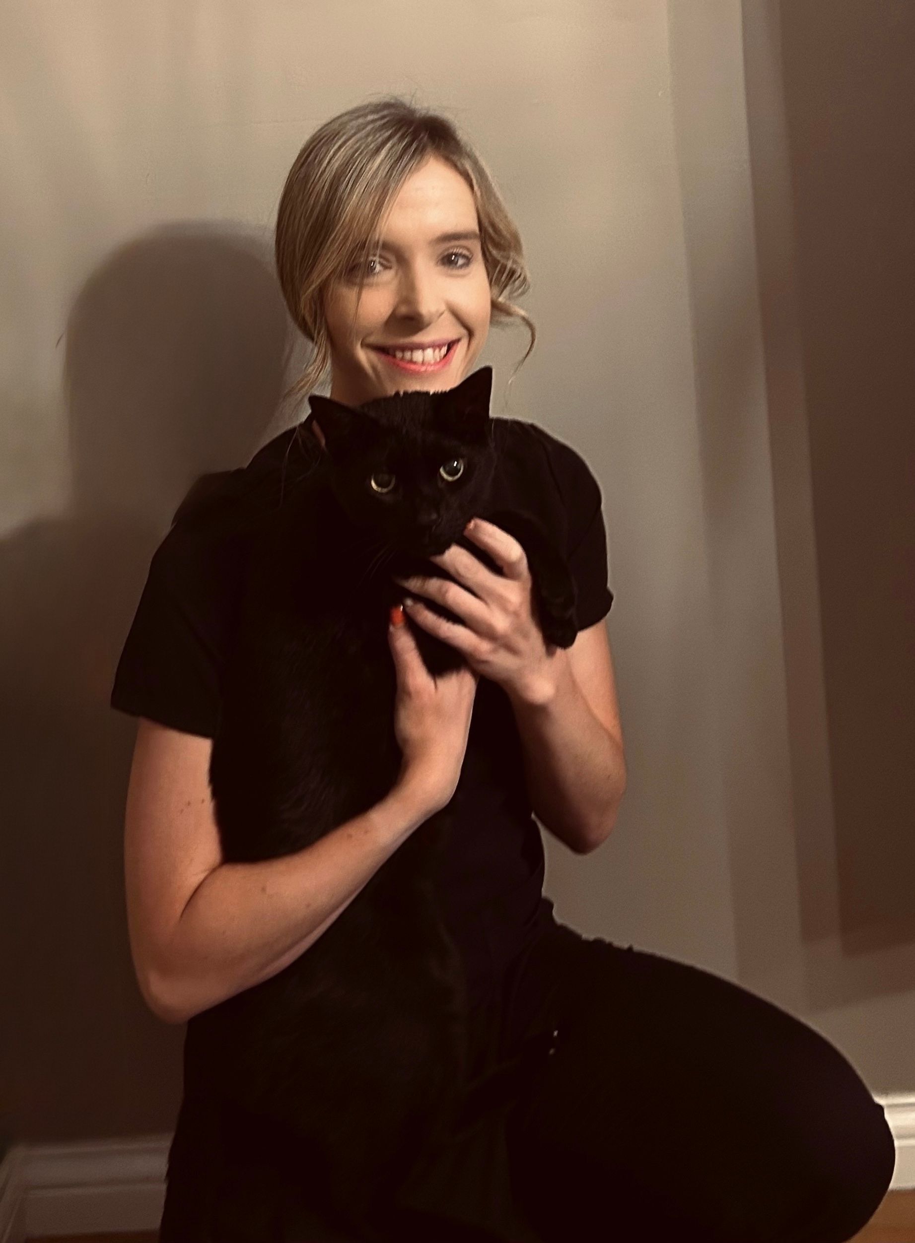 A woman is holding a black cat in her arms and smiling.