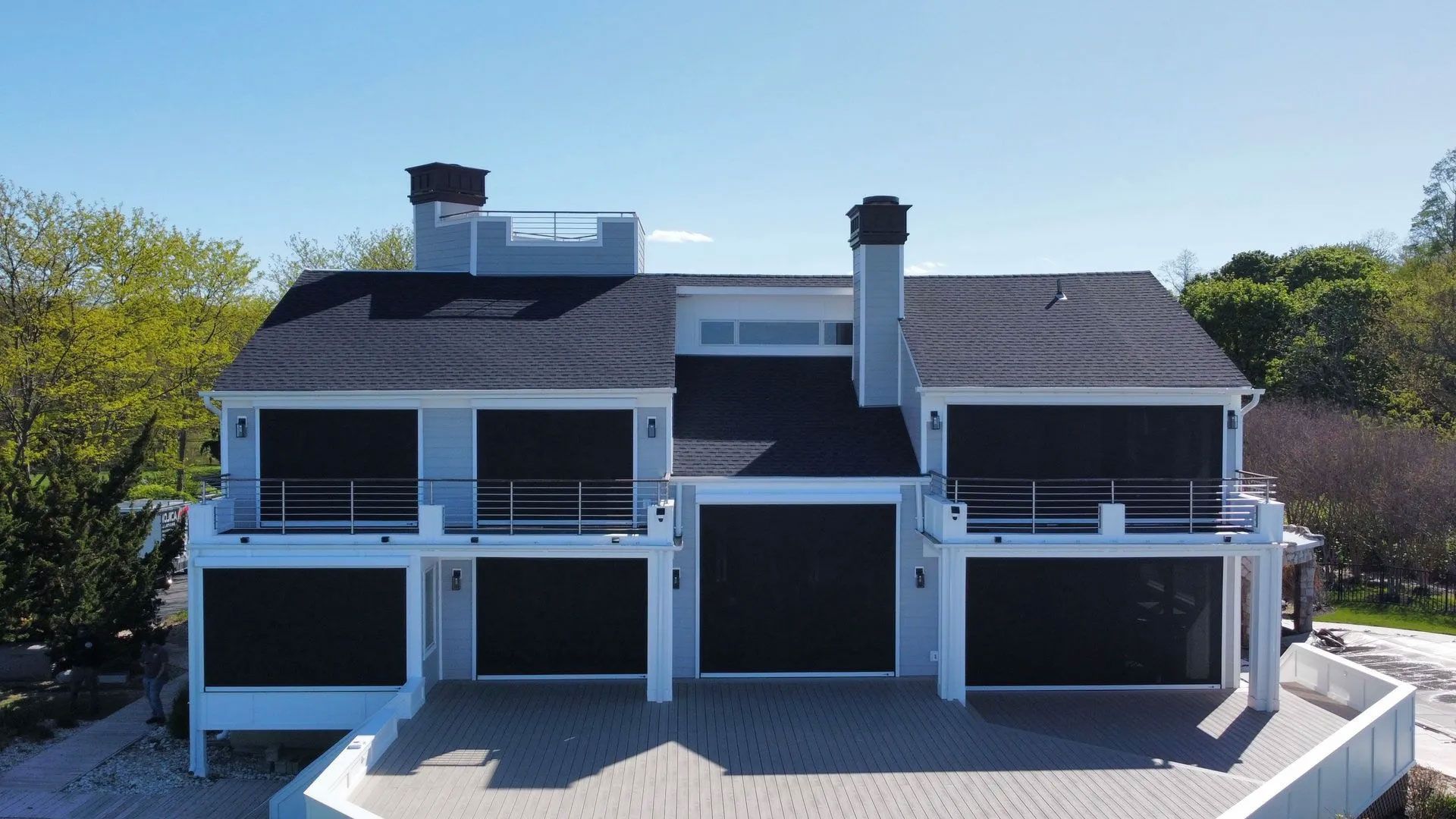 Large white waterfront house with balconies, dark roof, and a clear blue sky
