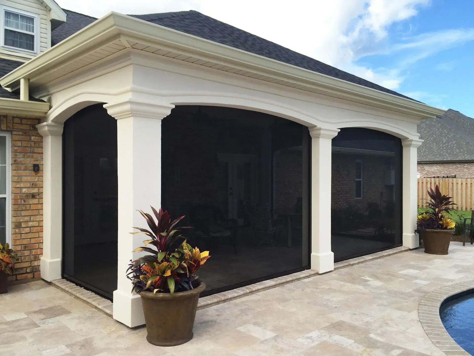 Screened patio with white columns, potted plants, and stone deck beside a house