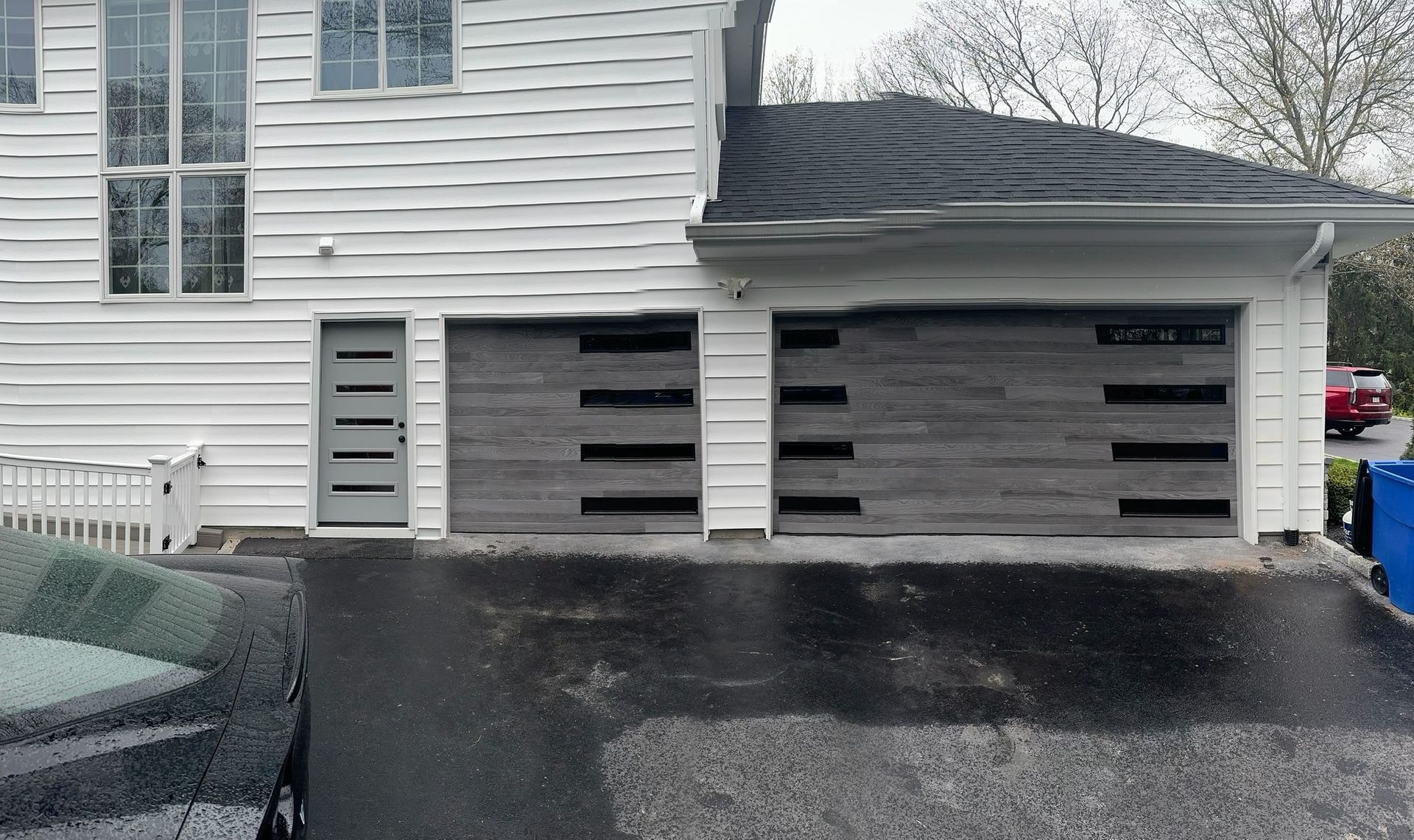 Two-story white house with gray garage doors. Black asphalt driveway. Gray entrance door.