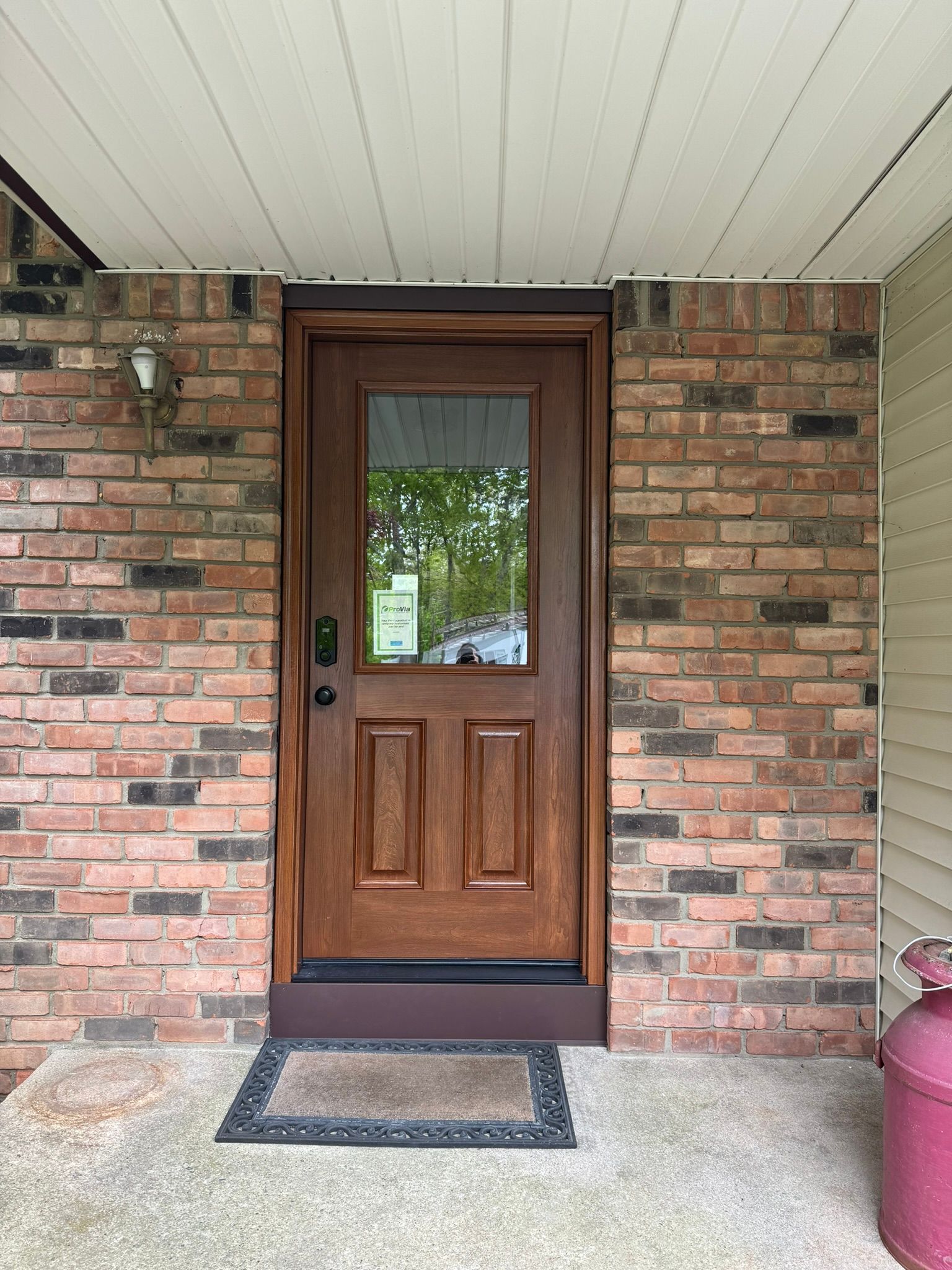 Brown door with glass panel set in brick wall, covered porch.