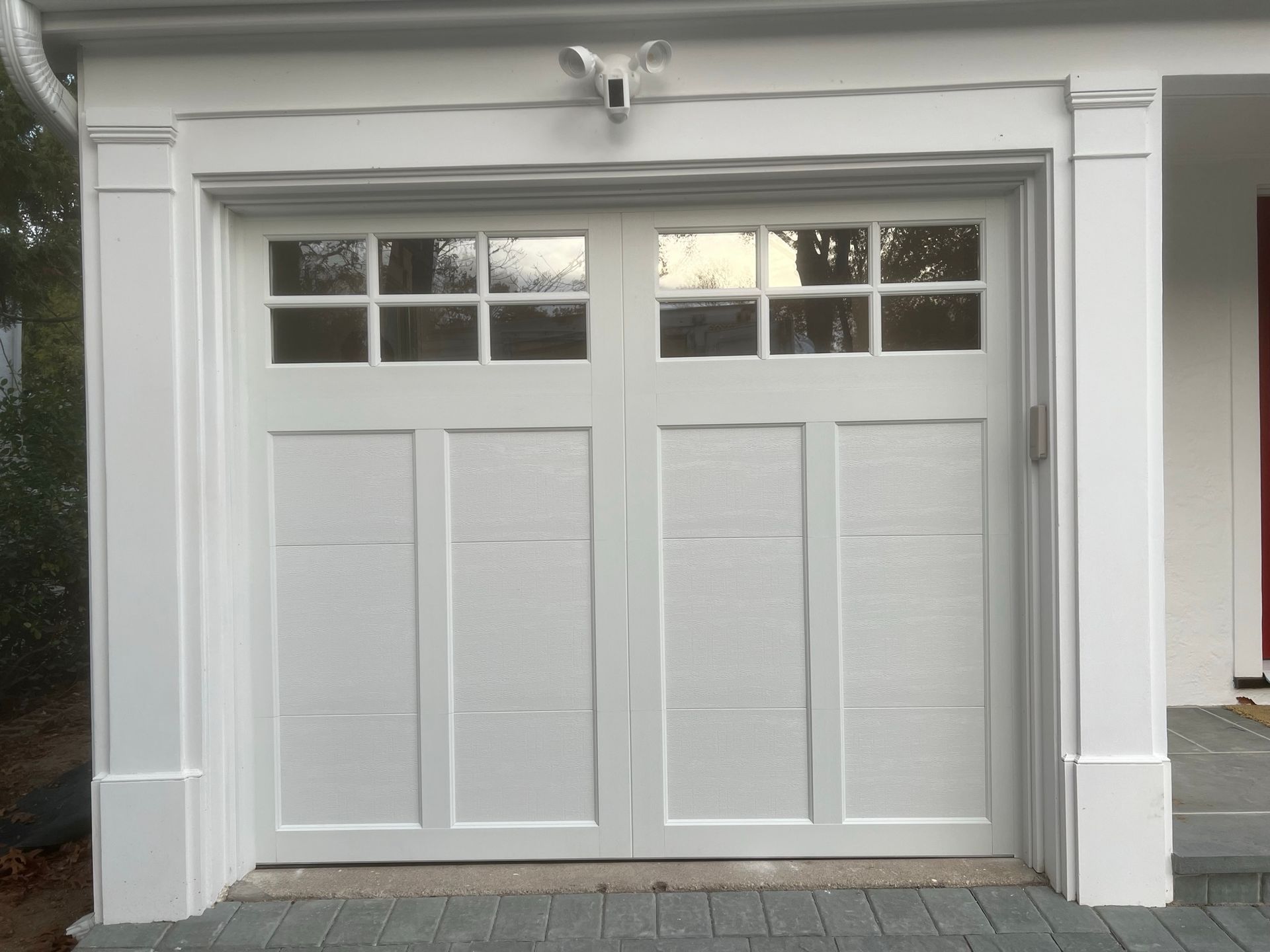 White two-car garage door with glass panes, framed in white trim, and a gargoyle accent above.
