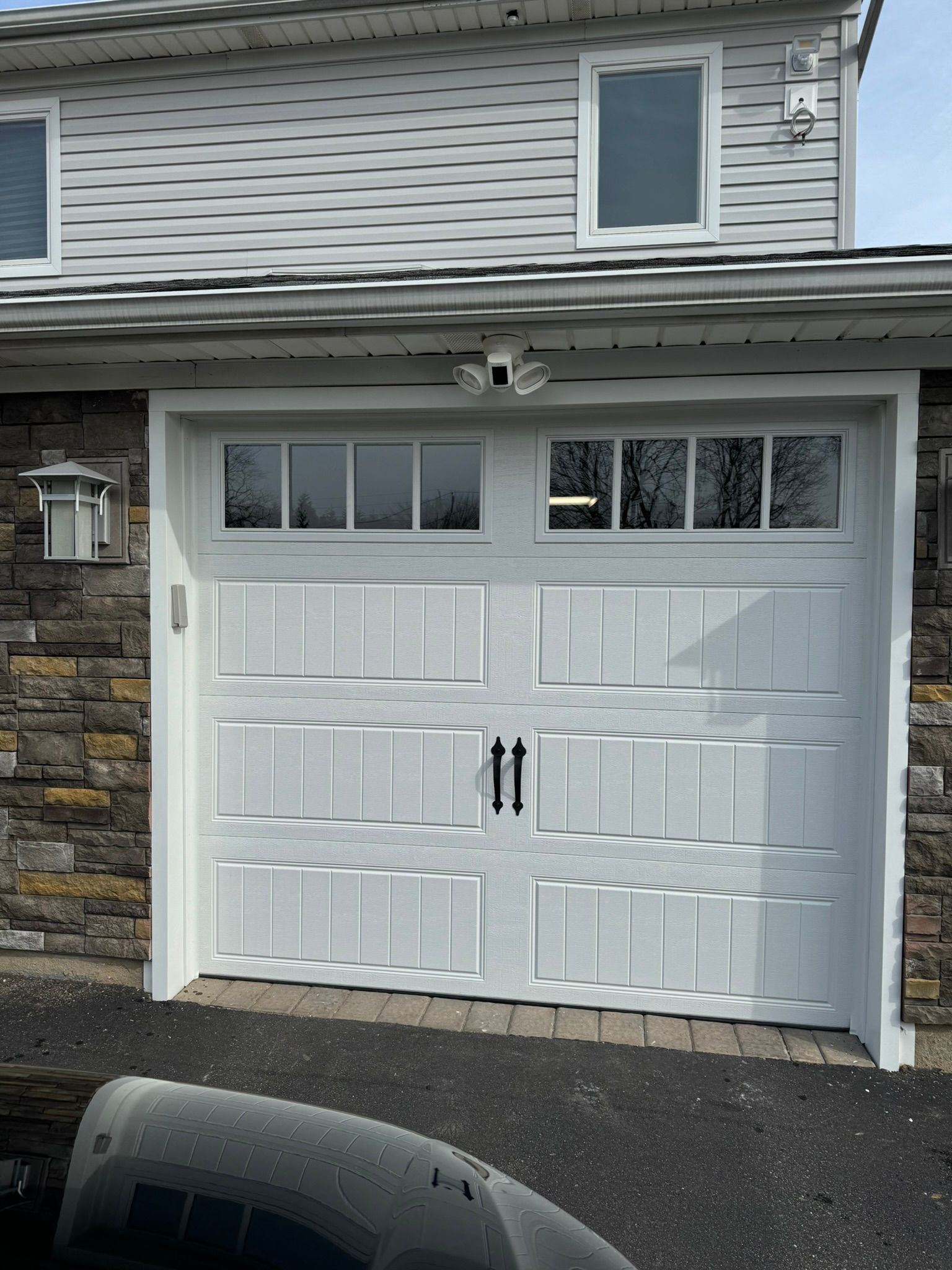 White garage door with windows, flanked by stone walls, under a gray roof.