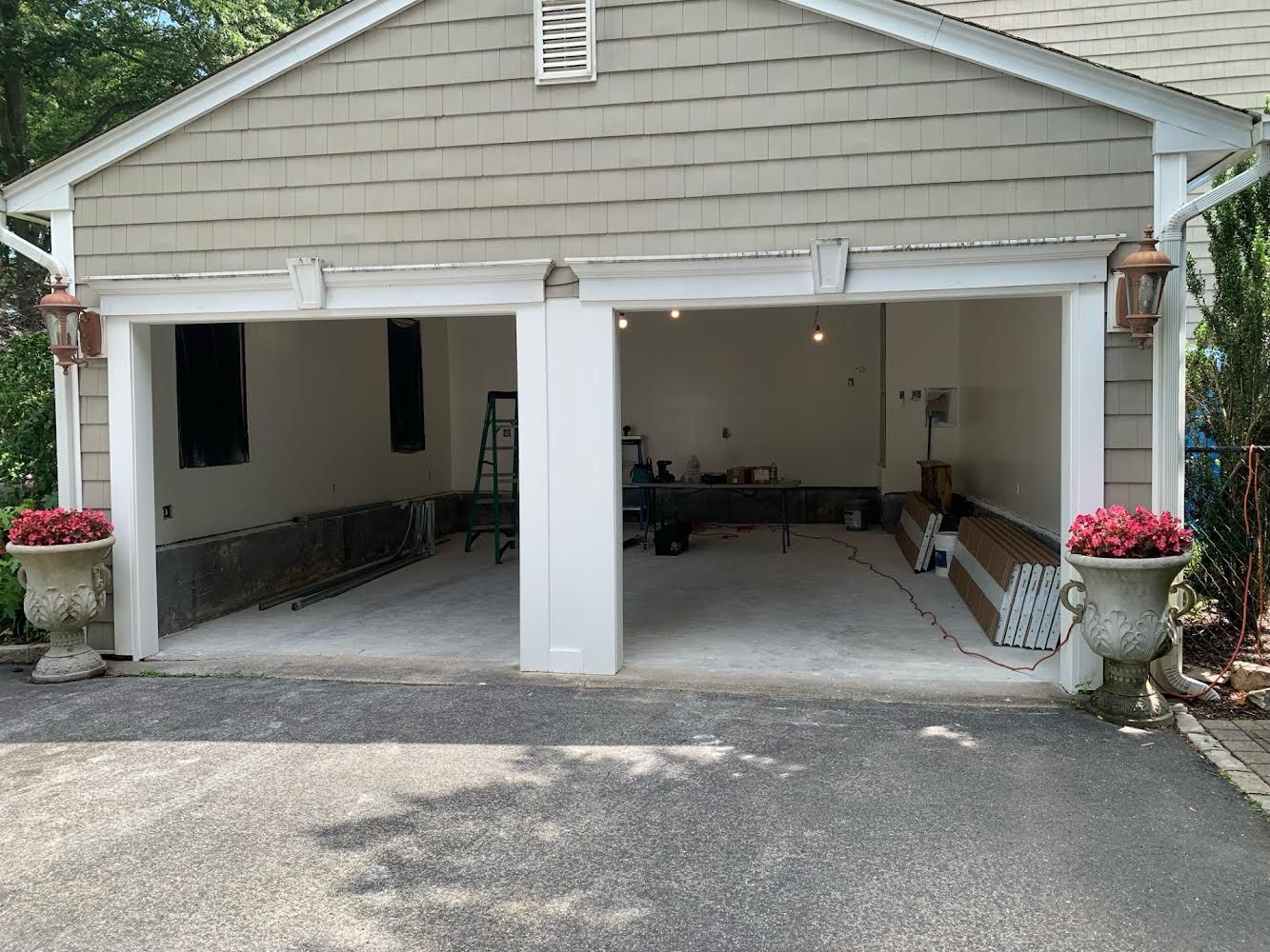 Two-car garage with open doors, freshly painted walls, and concrete floor. Flower pots flank the entrance.
