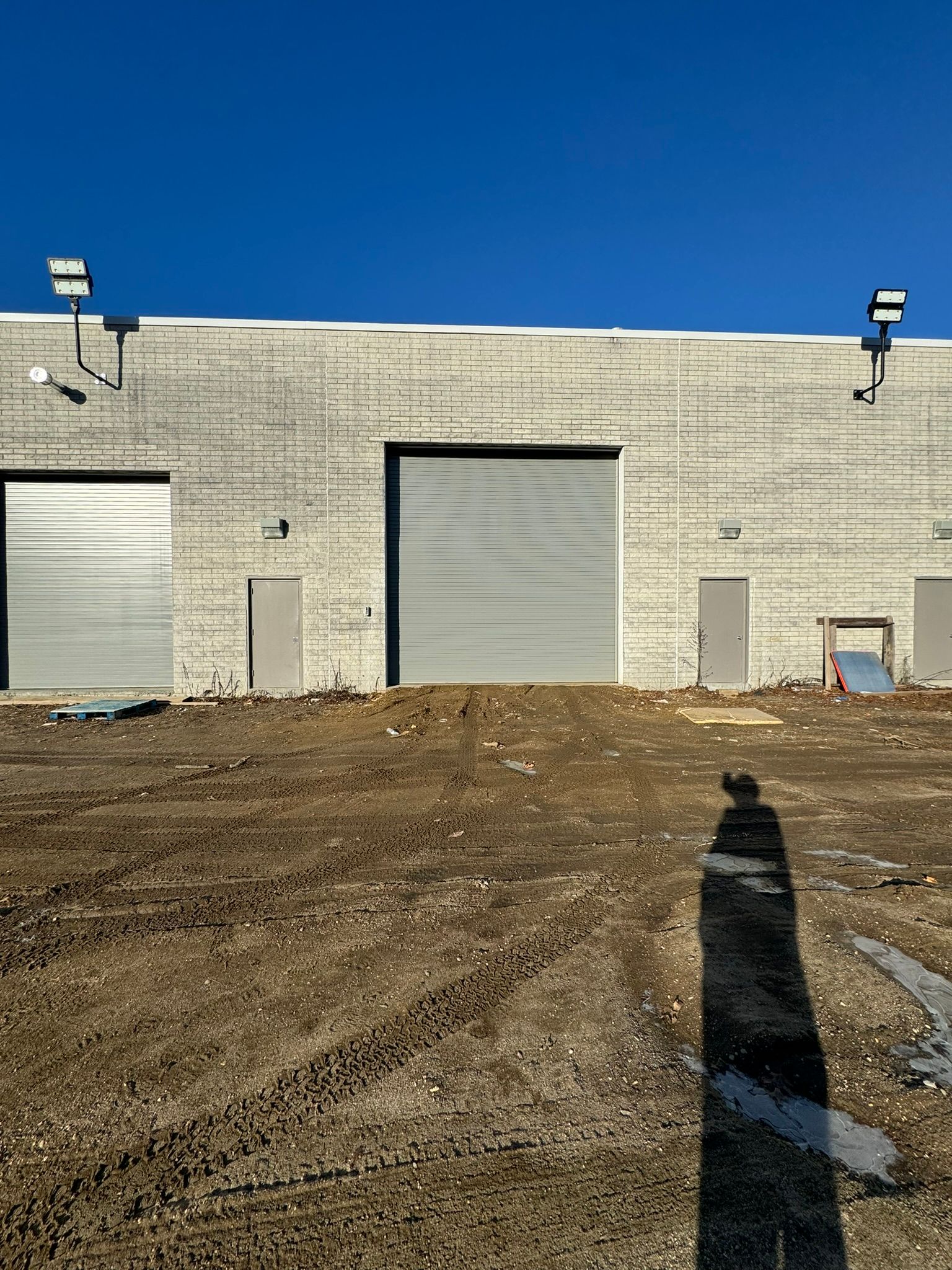 Warehouse exterior with three gray garage doors, light-colored brick, and blue sky.