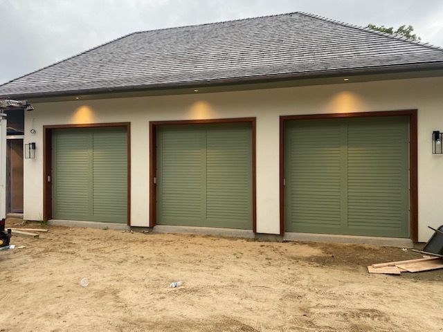 Three-door garage with green doors, wood trim, and a gray roof; set in a yard.