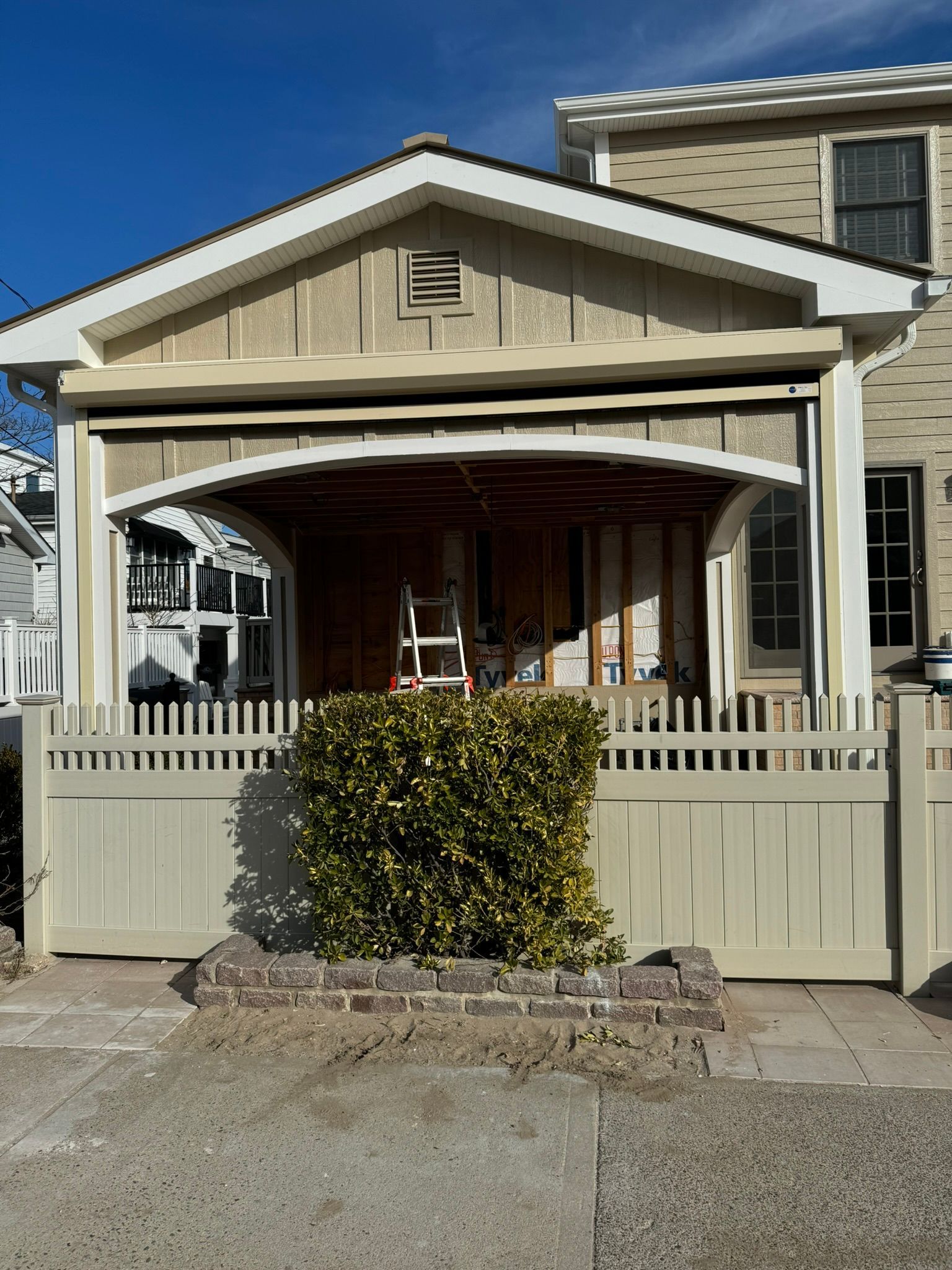Exterior view of a house undergoing construction with a picket fence and small brick planter.