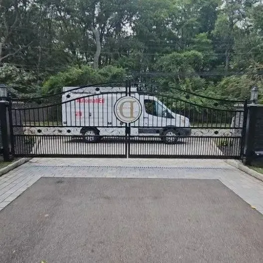Black gate with a white van behind it. The gate is in front of a driveway. 