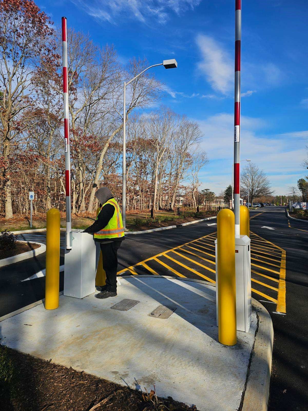 Person in safety vest operates gate arm at entrance to road.