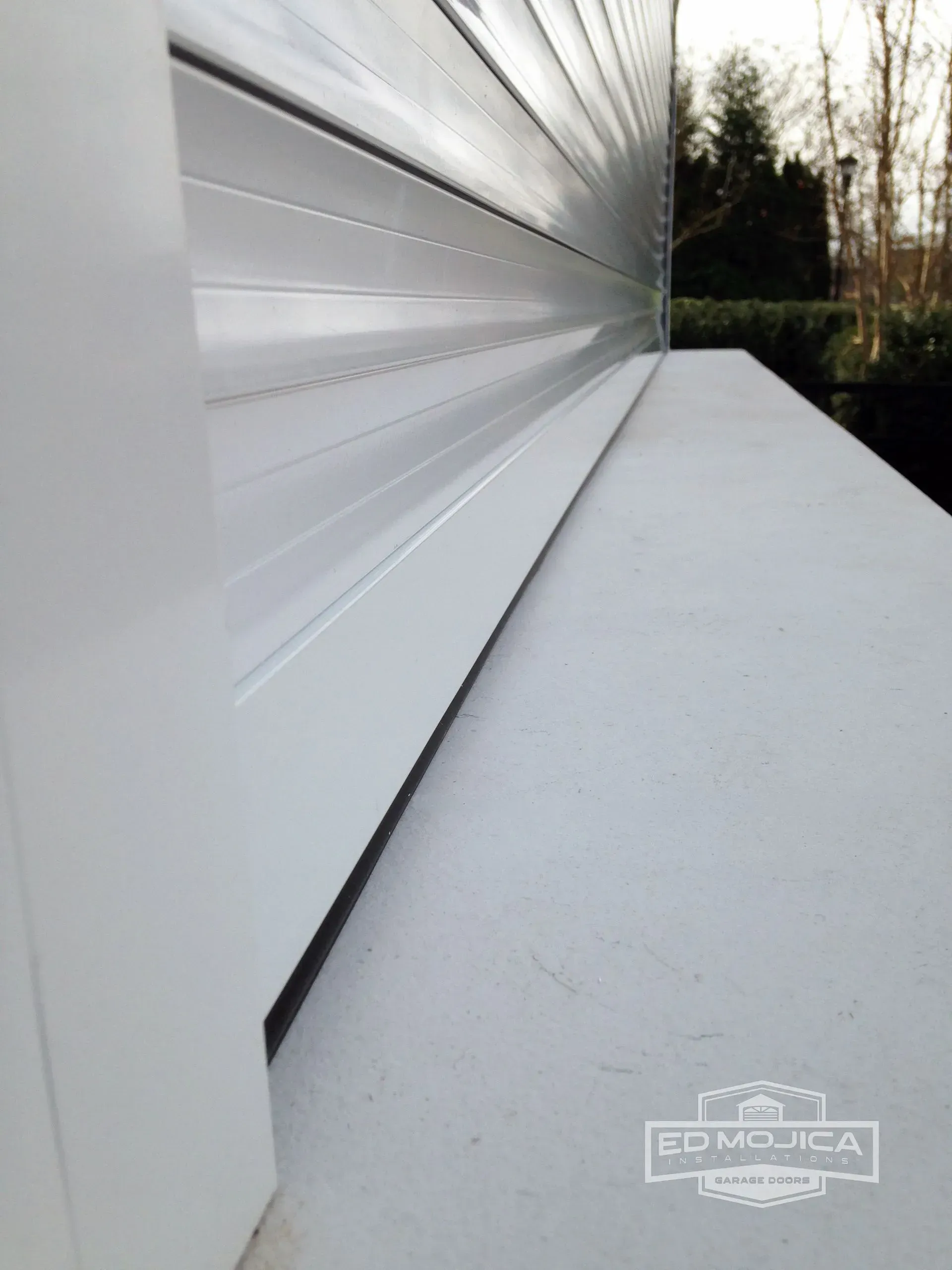 White building corner with a partially rolled-up silver shutter. Outdoors, natural light.