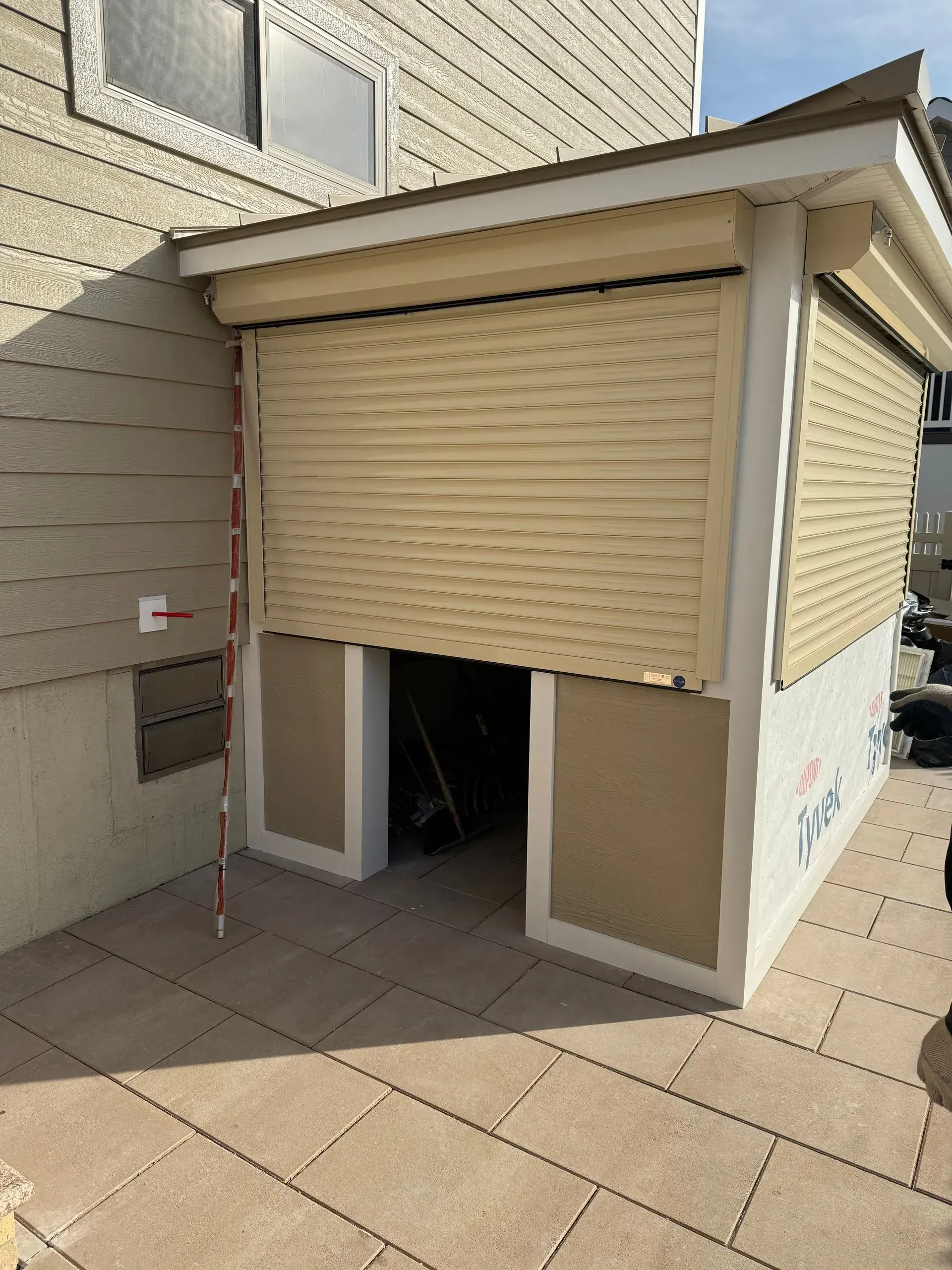 Beige roll-up security shutter over an open doorway on a patio, attached to a beige house exterior.