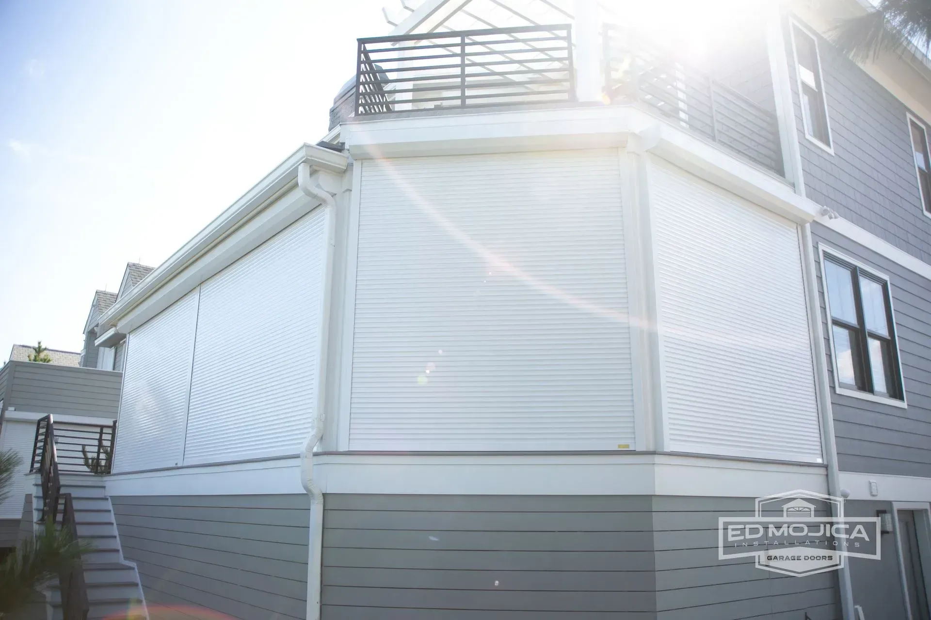 Exterior of a house with white paneling and gray siding, featuring roll-down white shades.