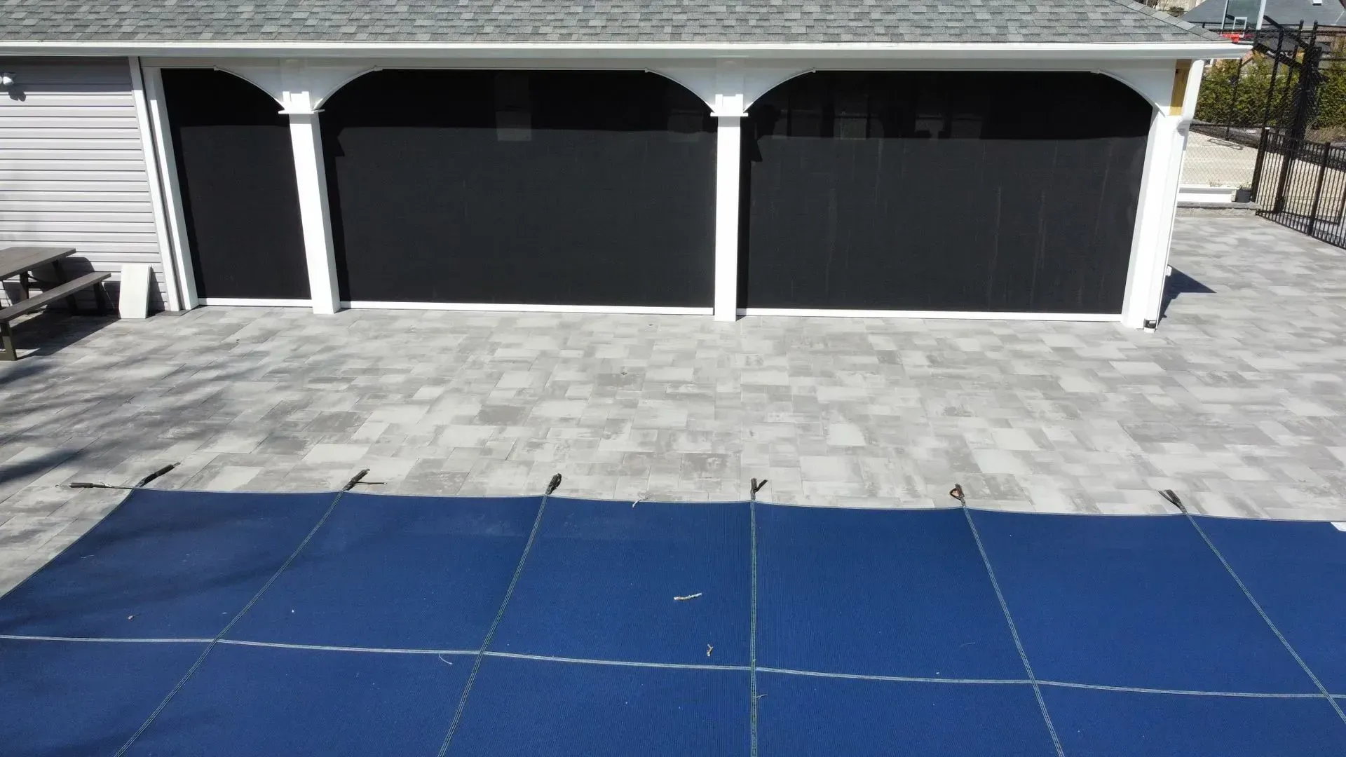 Blue pool cover on gray patio in front of a white covered structure with black screens.