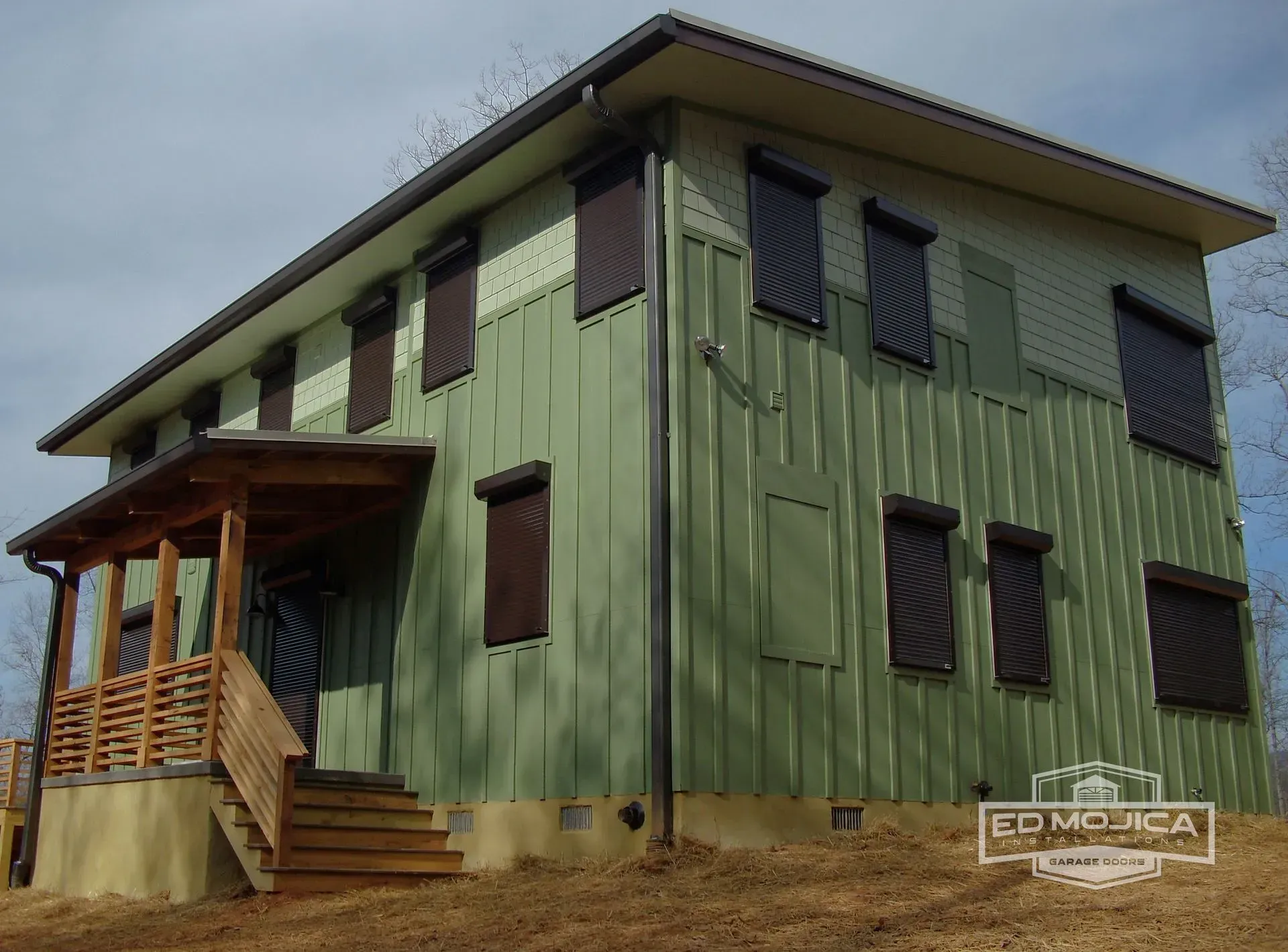 Two-story green house with brown shutters and porch on a sunny day.