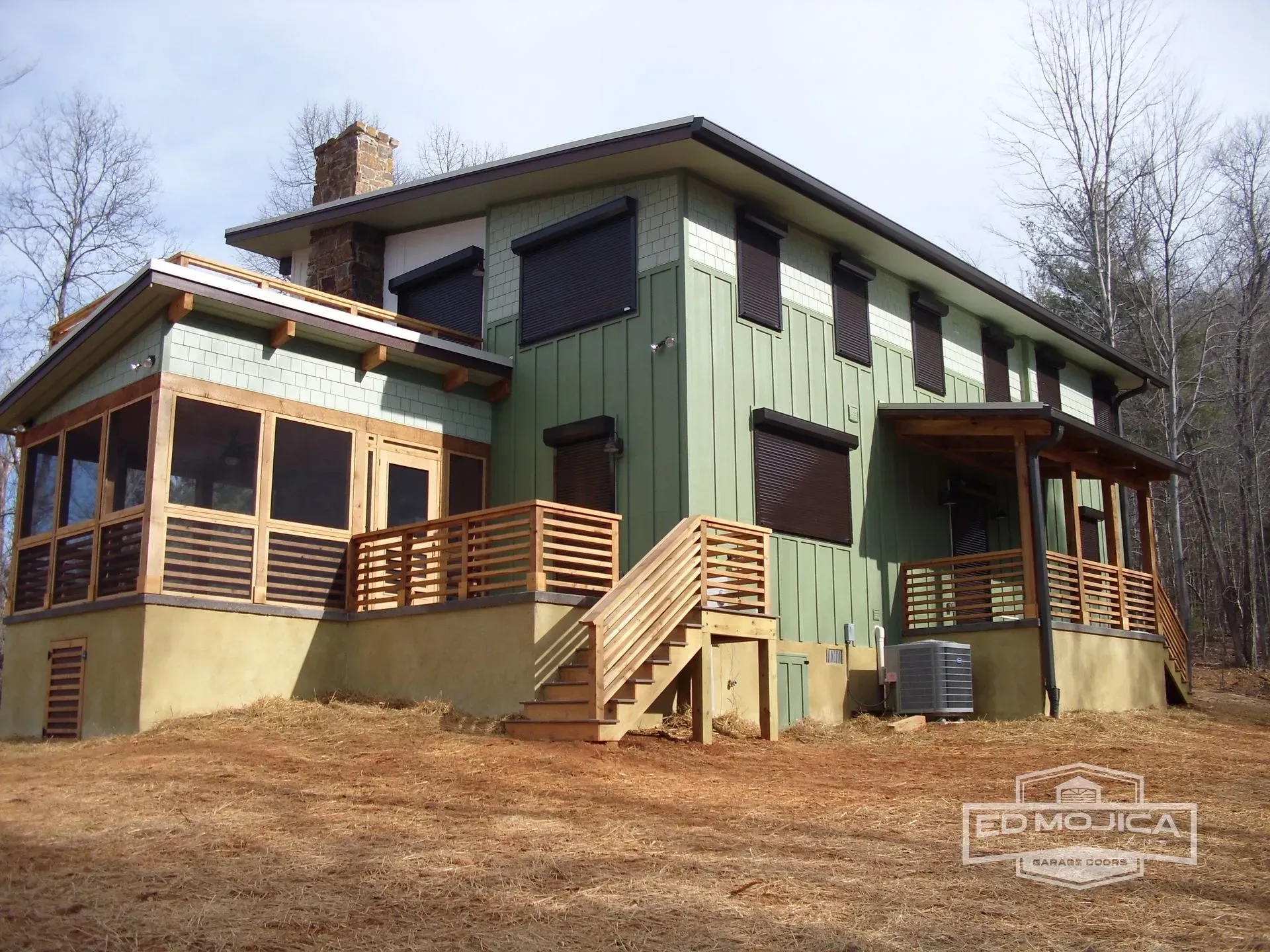 Two-story house with screened porch, wooden deck, and brown shutters on green siding. Brown wooden stairs lead up.
