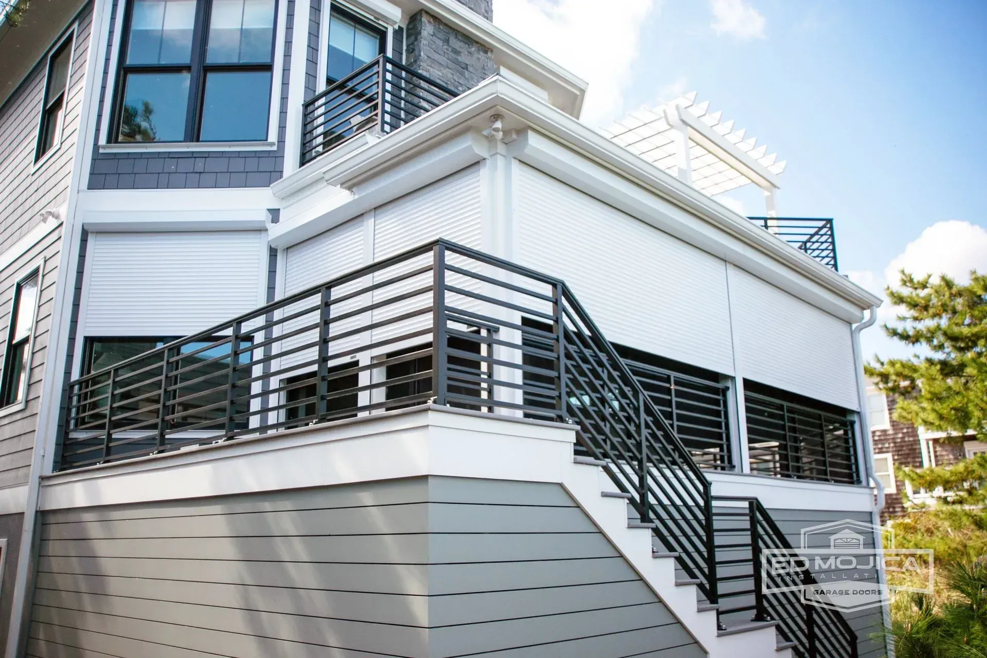 White and gray house exterior with a deck, stairs, and dark metal railings.