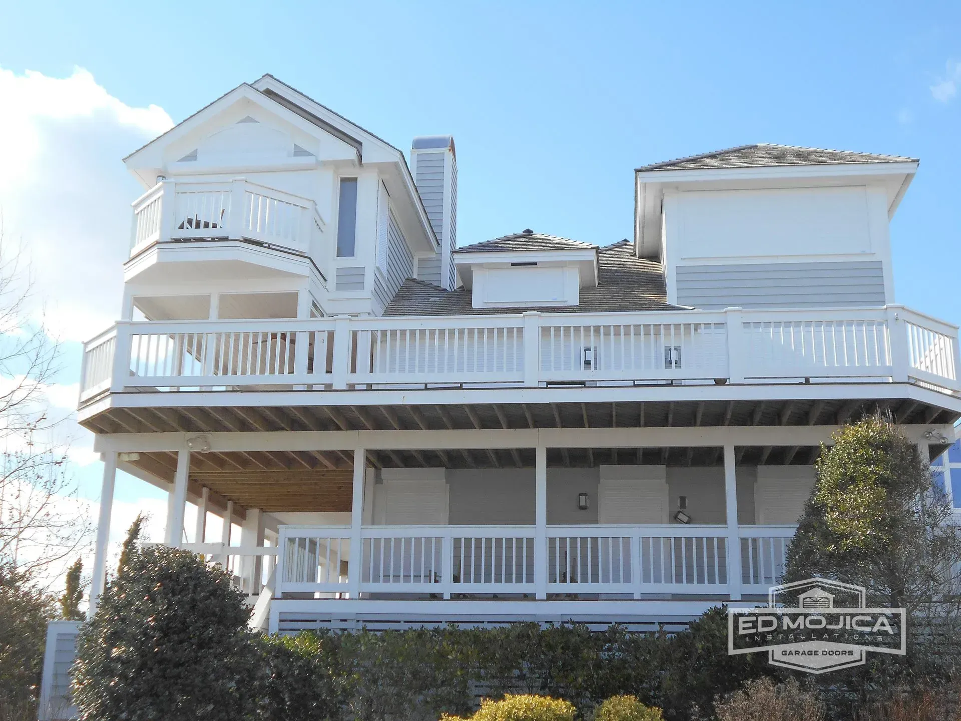 White multi-level house with large decks, a light blue sky.