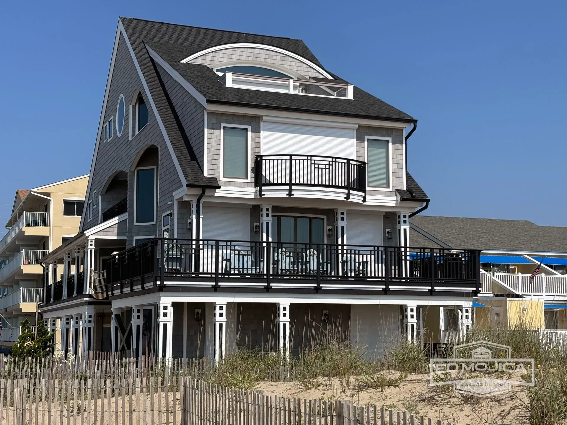 Beachfront home with gray siding, black railings, and a small porch on a sunny day.