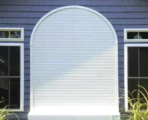 White arched shutter covering large window; flanked by two rectangular windows on blue siding.