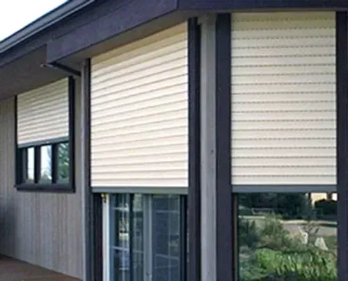 Exterior view of a building with three windows; each has closed, beige, rolling shutters.