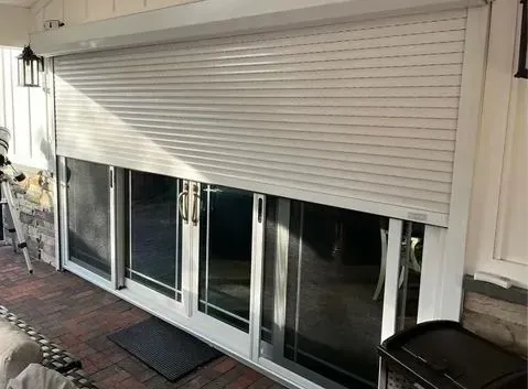 Exterior view of white roll-down shutter partially covering sliding glass doors on a porch.