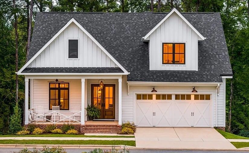 White farmhouse with black roof, brown door, and attached garage.