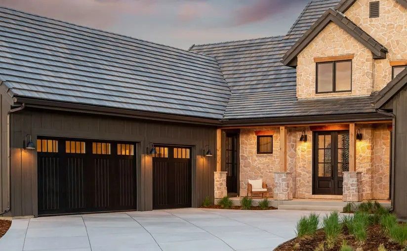 Modern home exterior with gray roof, black garage doors, and brick accents.
