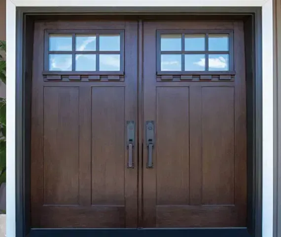 Brown double doors with square glass windows, dark handles, and a white frame.