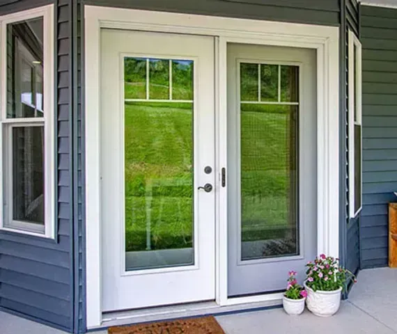 White French doors with screen door, reflecting green lawn.