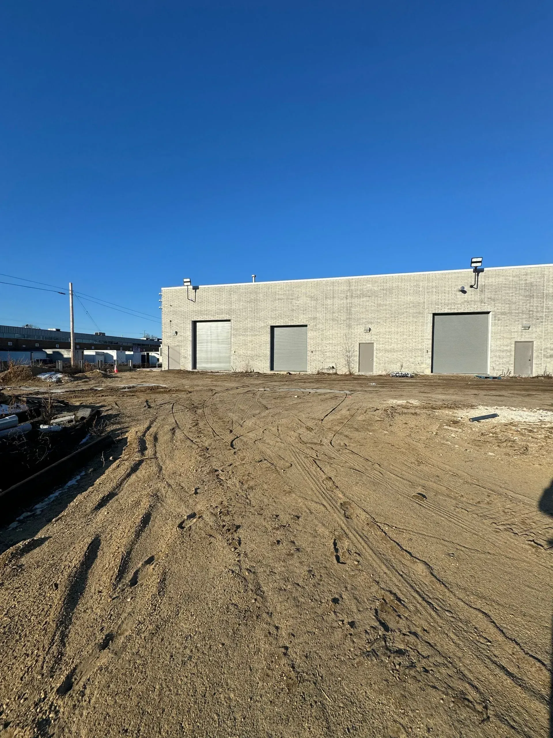 A gravel lot in front of a concrete building with three closed gray garage doors under a clear blue sky.