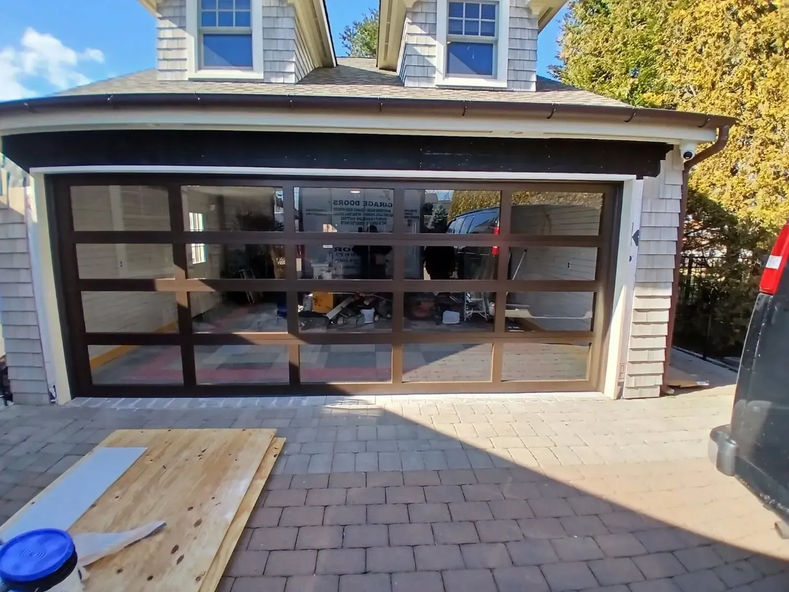 Garage with glass panels and brown trim. Pavers in front; blue sky visible above.