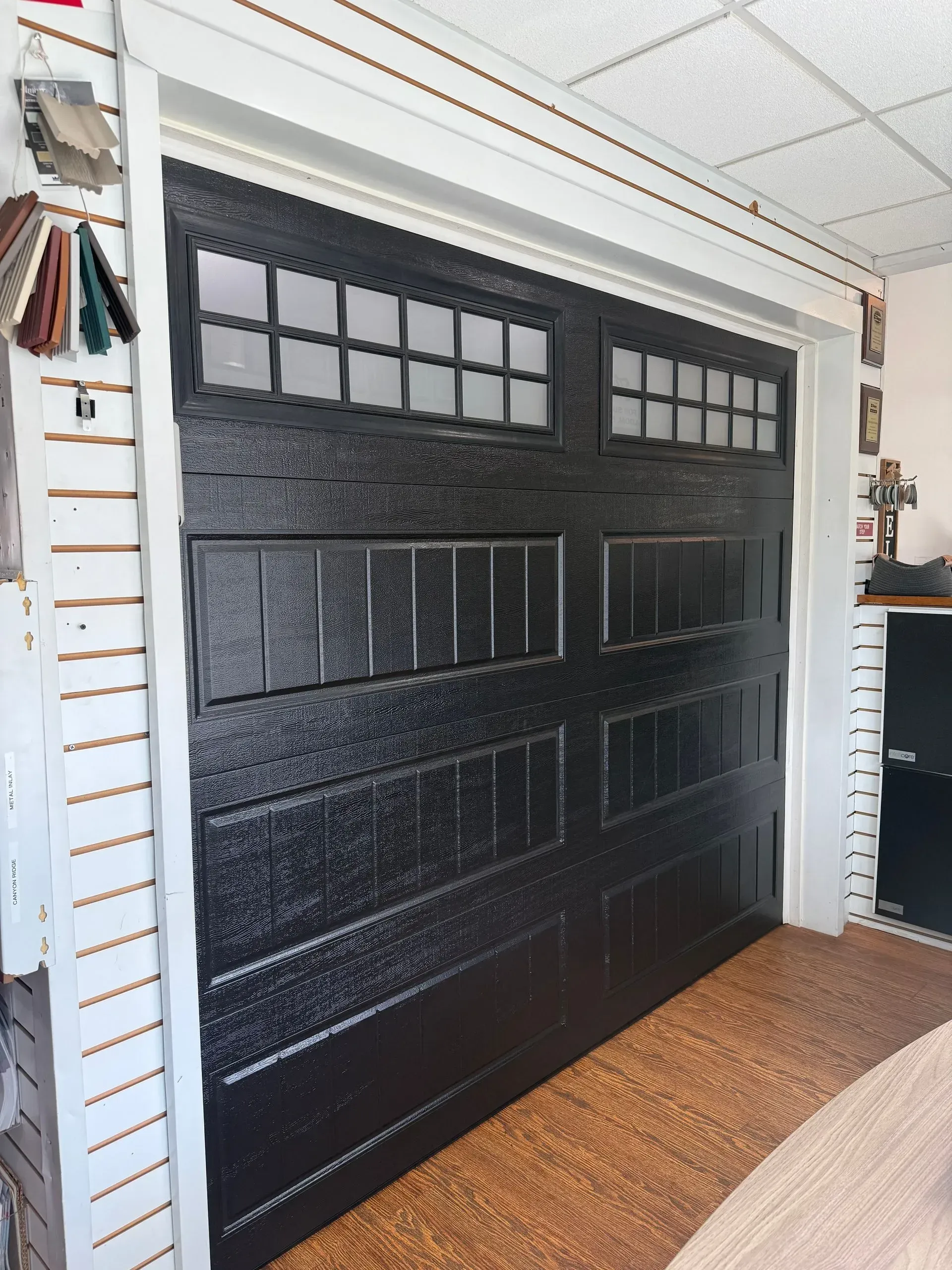 Black garage door with rectangular windows, displayed in a showroom.