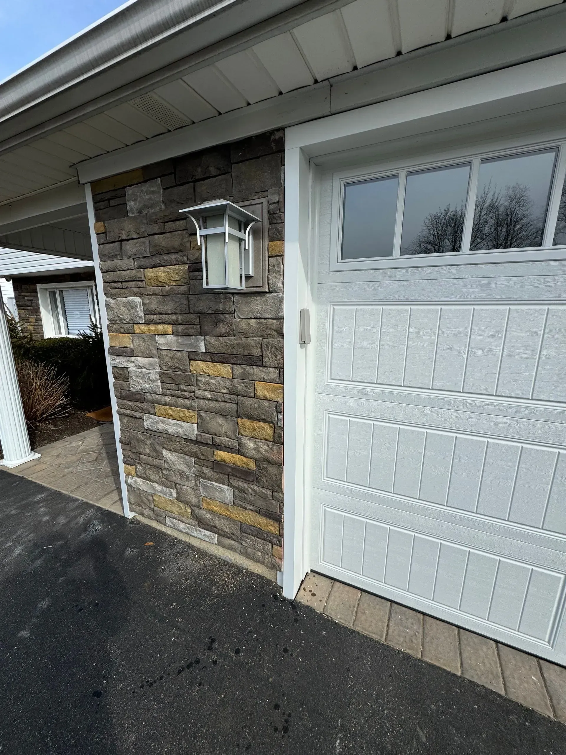 Garage exterior with stone accent wall and white garage door. Light fixture mounted on the wall.
