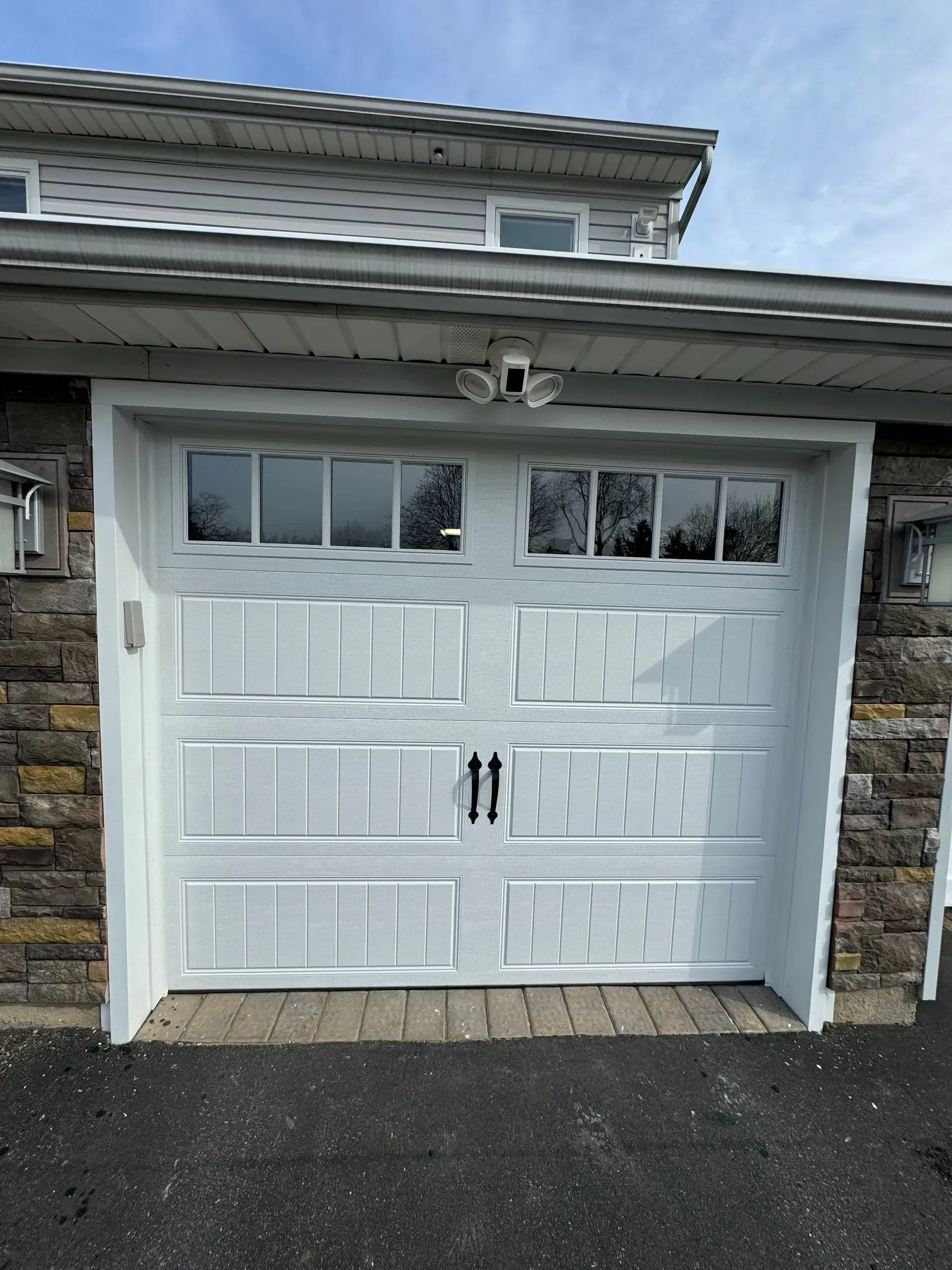 White garage door with windows, flanked by stone walls, under a clear sky.