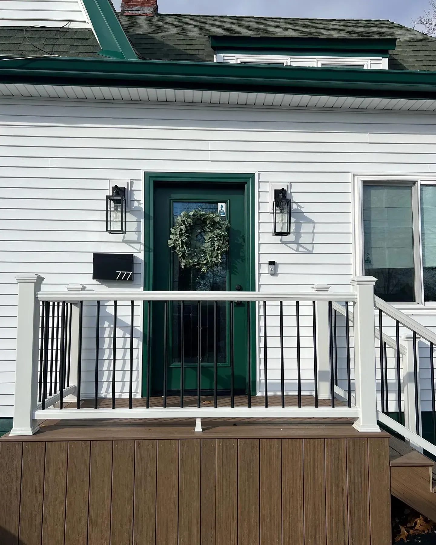 White house with green door, wreath, and porch. Black lights and mailbox.