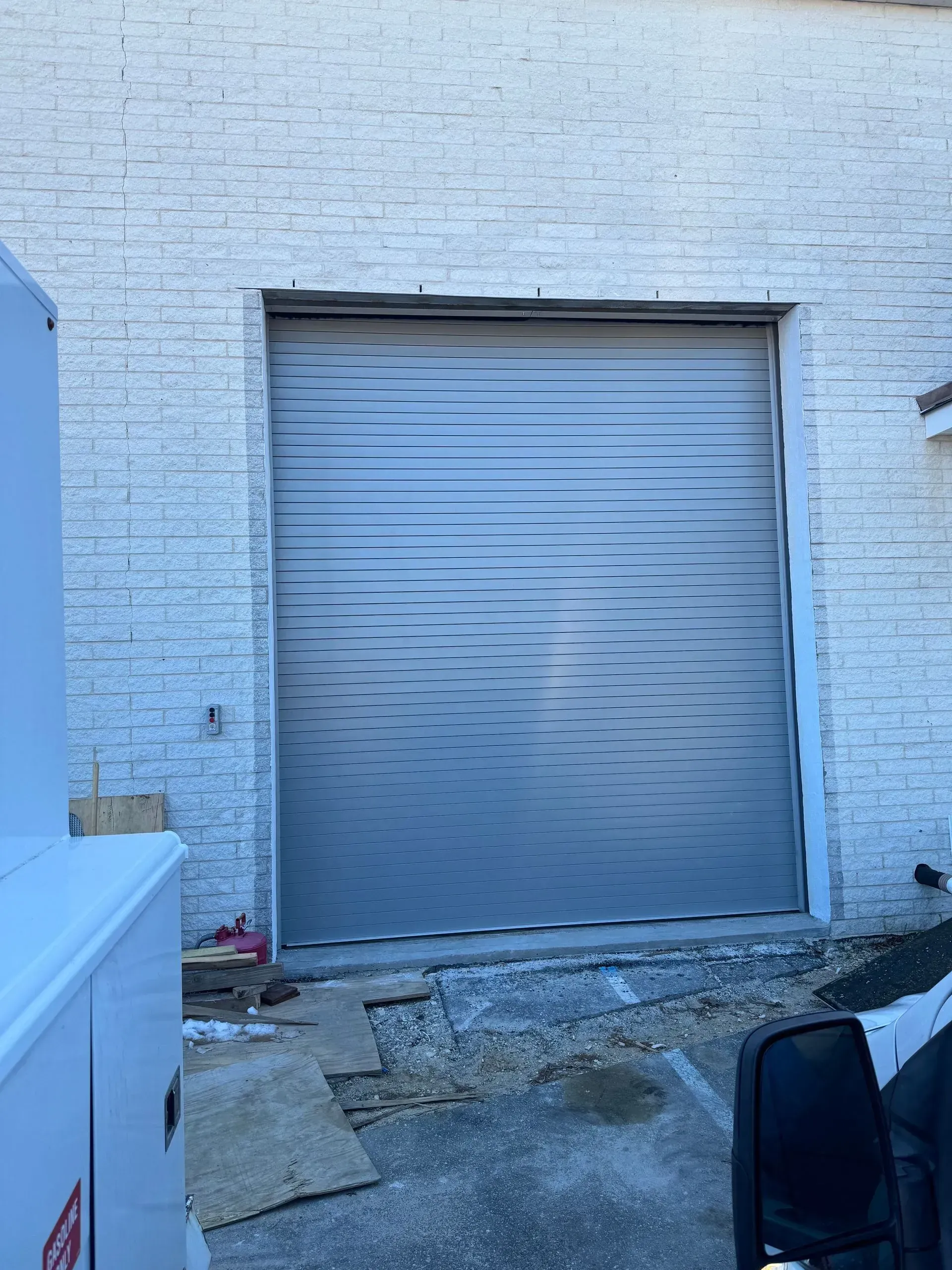 A closed, gray commercial roll-up door set in a white brick building.