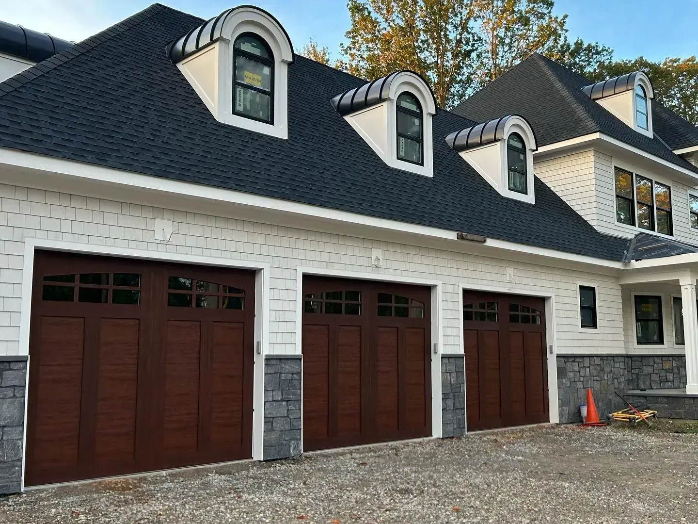 Exterior view of a white house with three brown garage doors, gray stone accents, and dark blue roof.