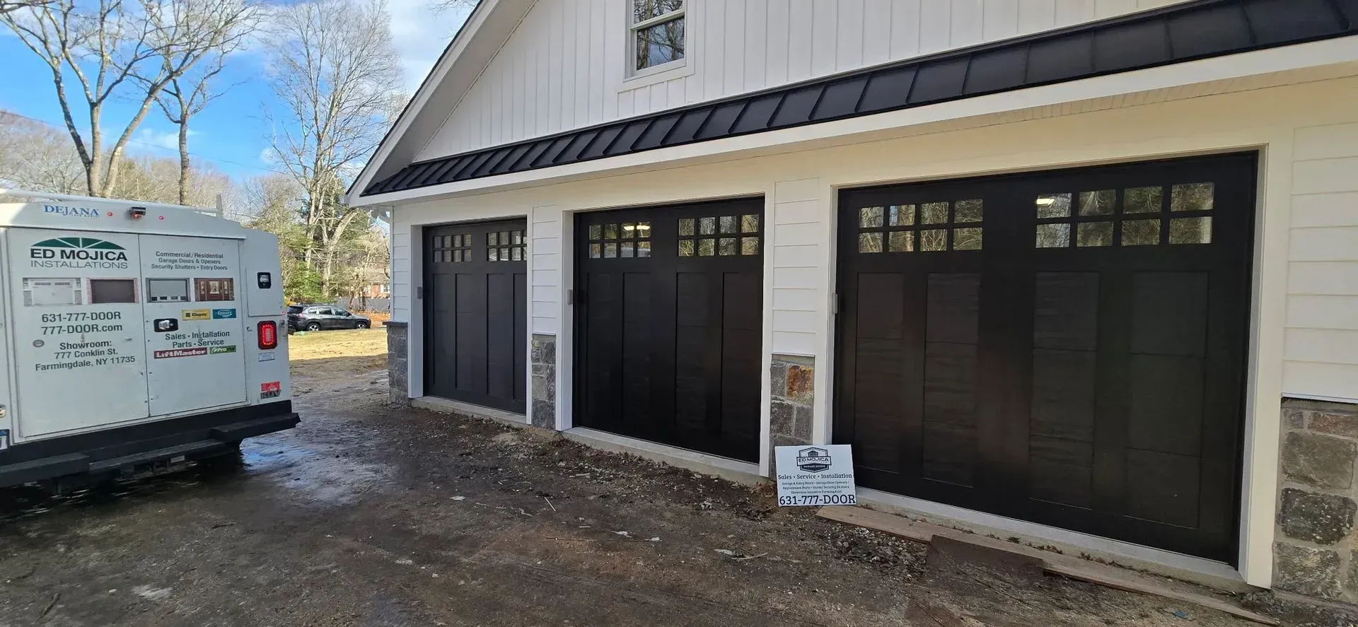Three dark garage doors on a white building with black trim. A white work truck is parked on the left.