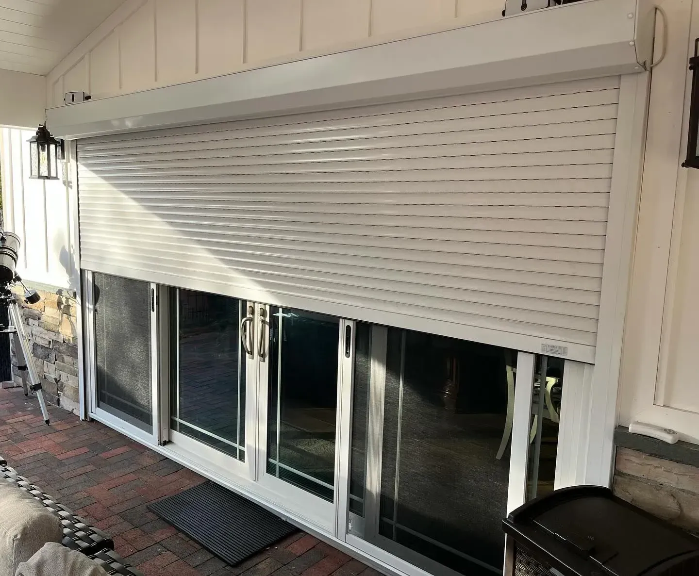 White rolling shutter covers a glass sliding door on a porch.