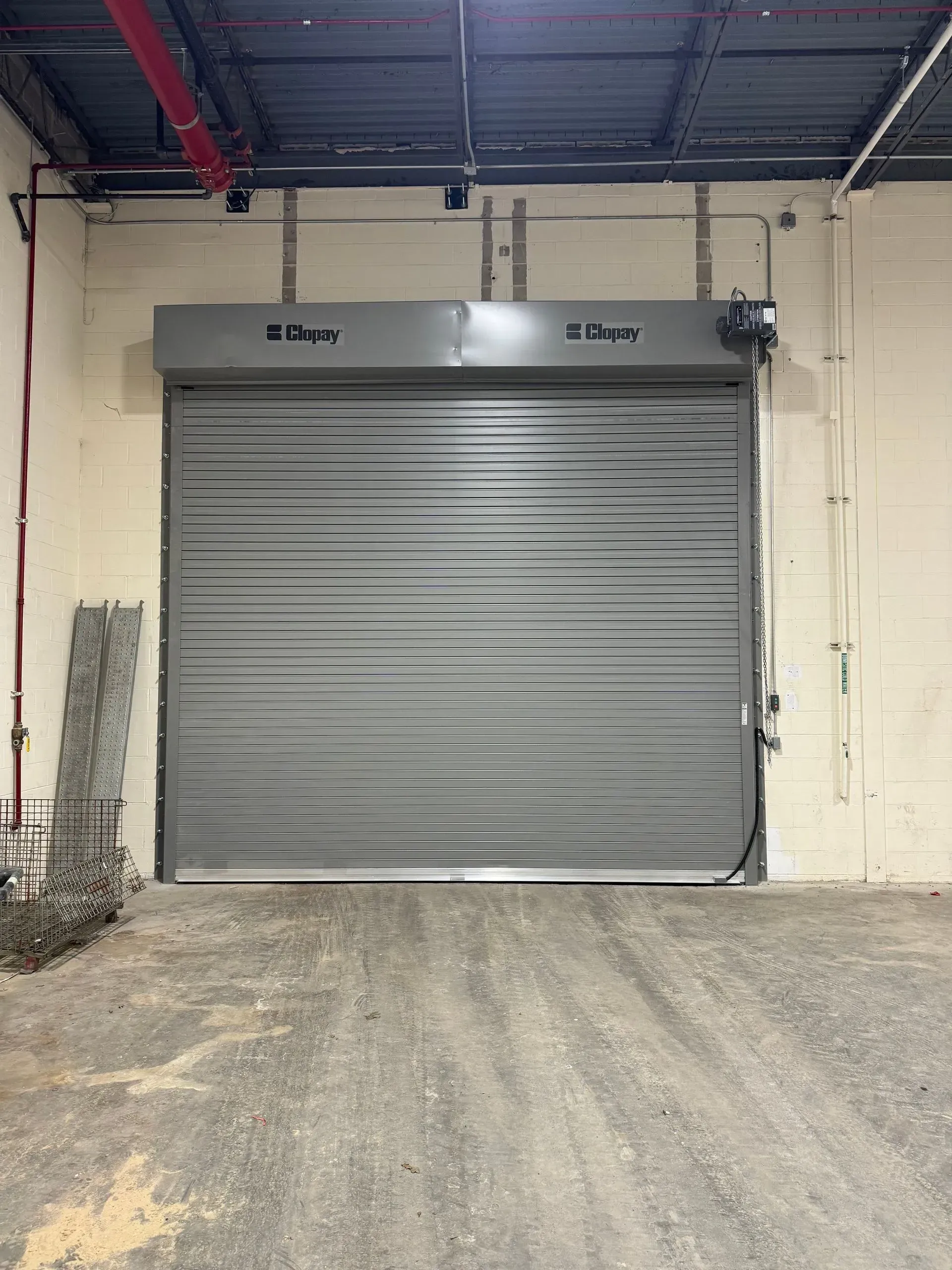 Gray industrial rolling shutter closed in a warehouse setting.