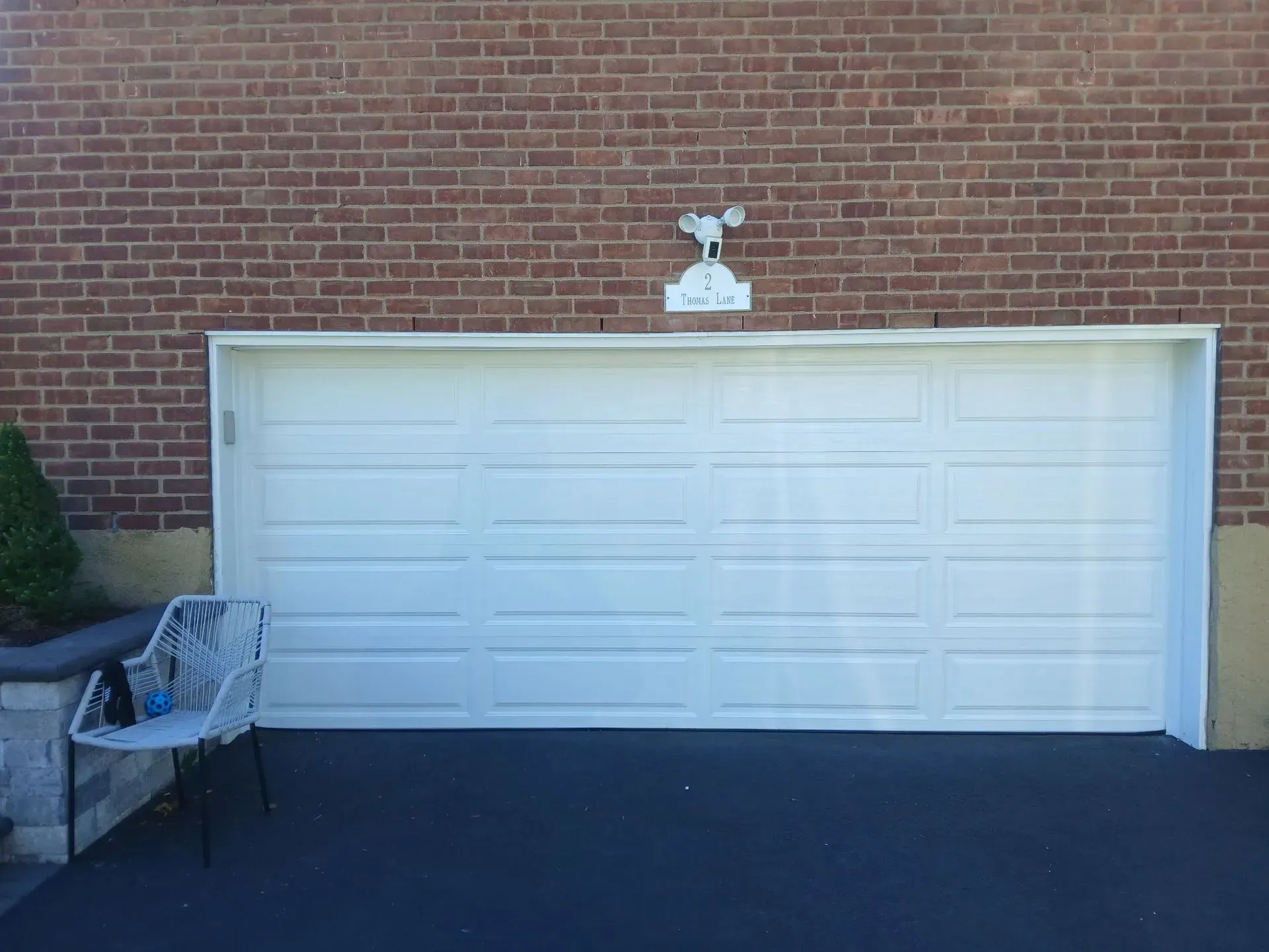 White garage door on brick building with a weathervane above it and a chair nearby.