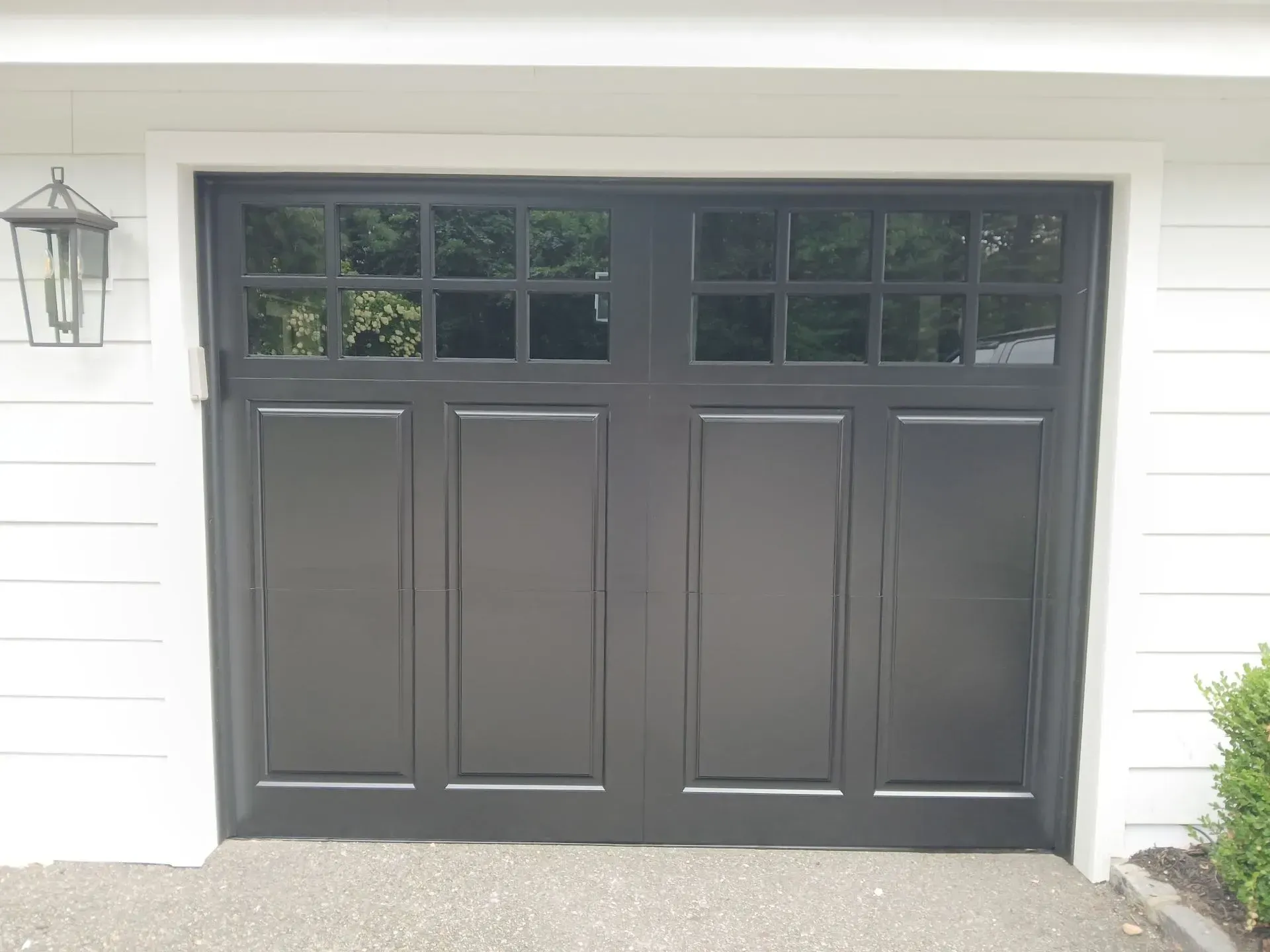 Black garage door with windowed top panels, framed in white, next to a white exterior wall.