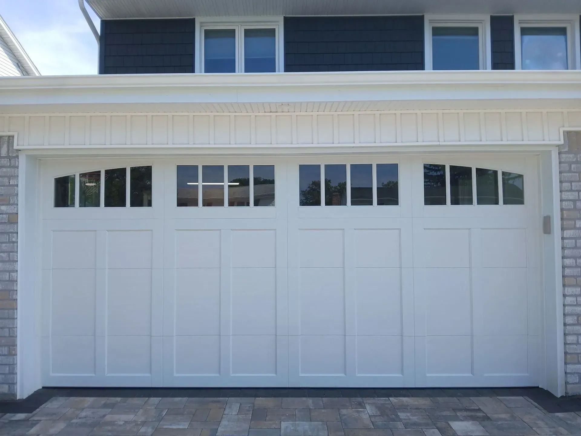 White garage door with glass paneling, brick accents, and blue siding above.