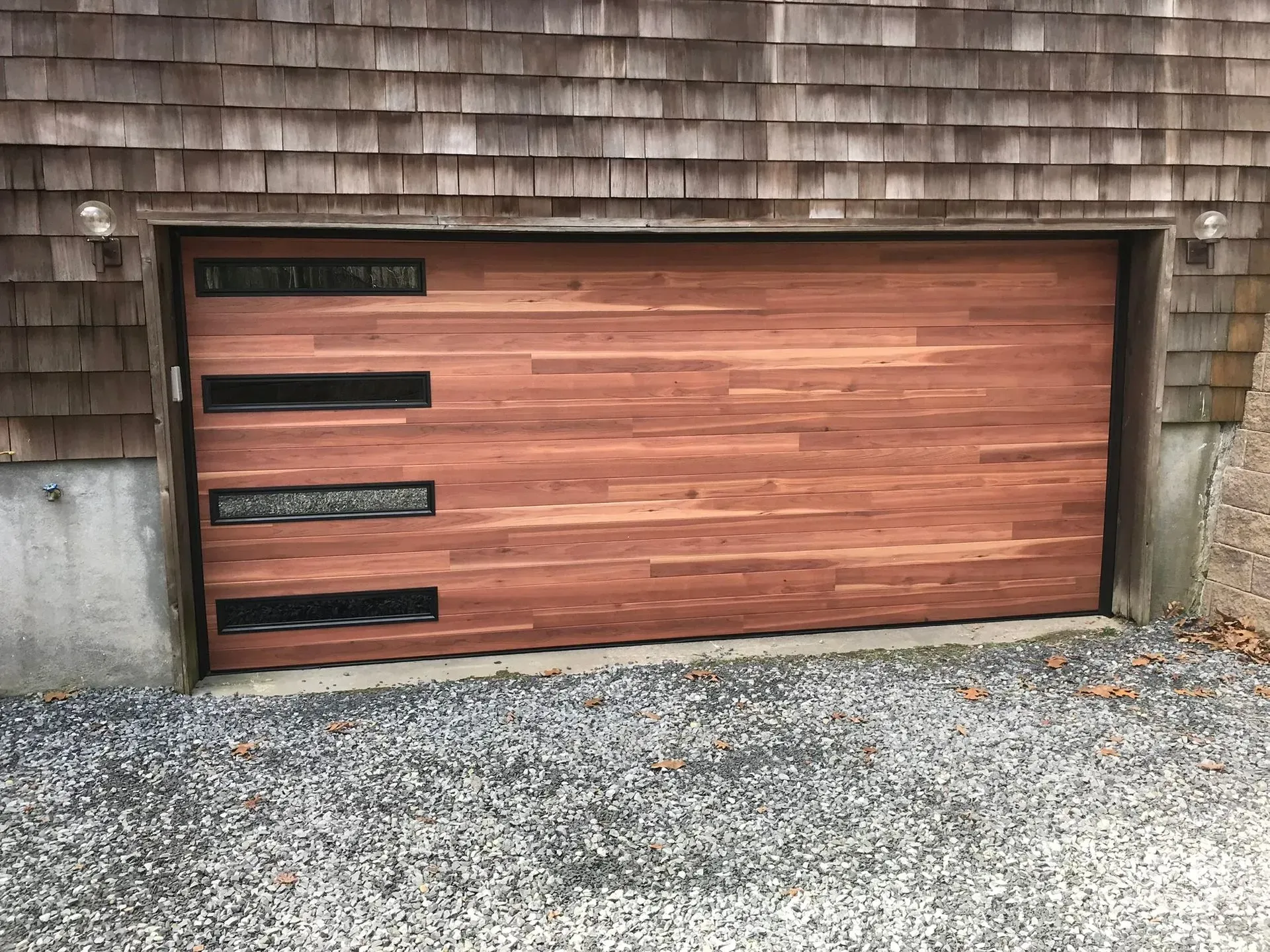 Wooden garage door with horizontal planks, three black window panels, on gravel.