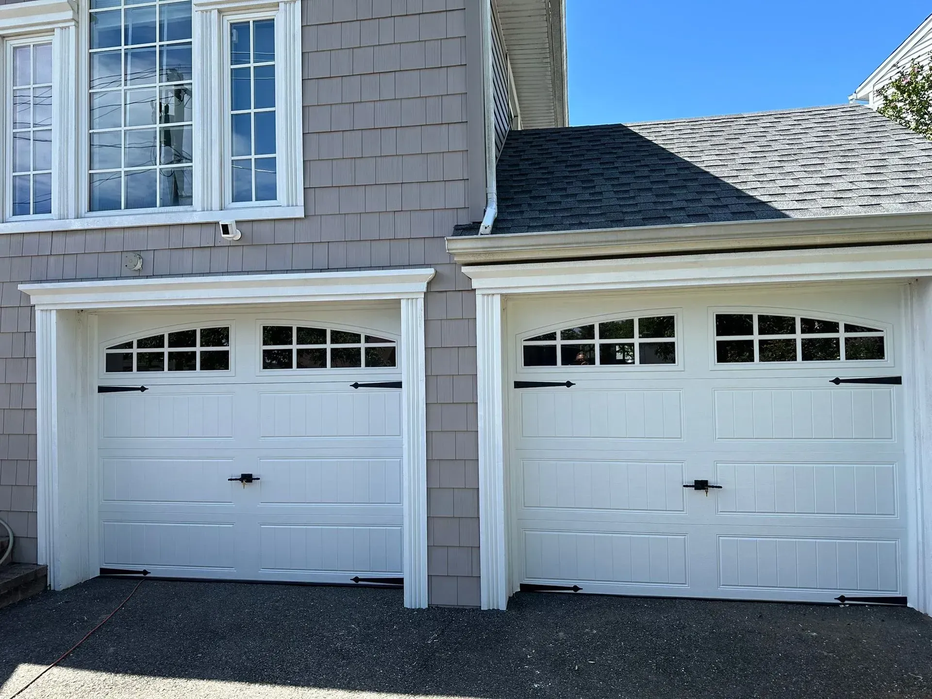 White garage doors with arched windows; house exterior, gray siding.