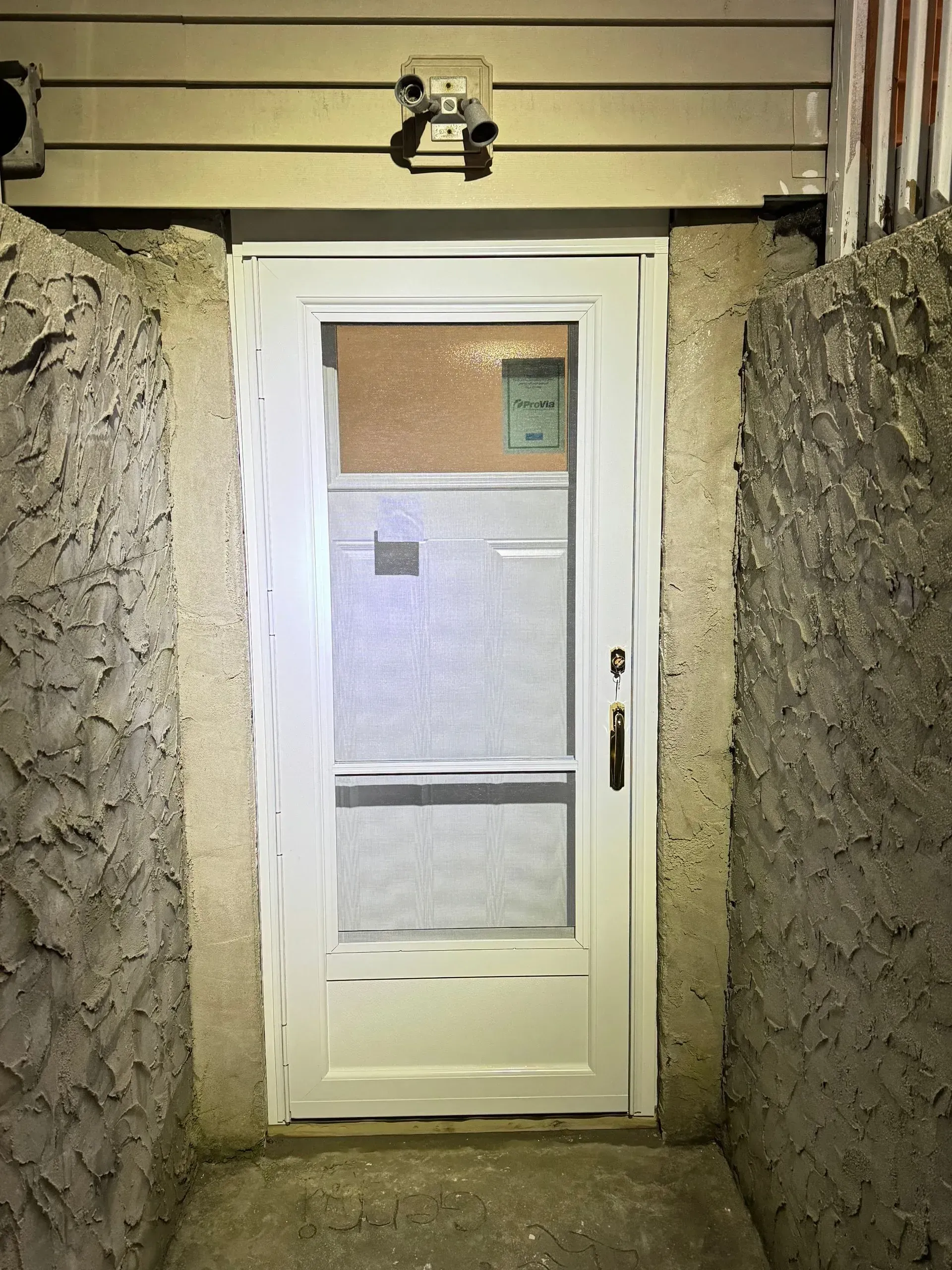 White-framed door with a screen, between textured walls, beneath a light fixture.